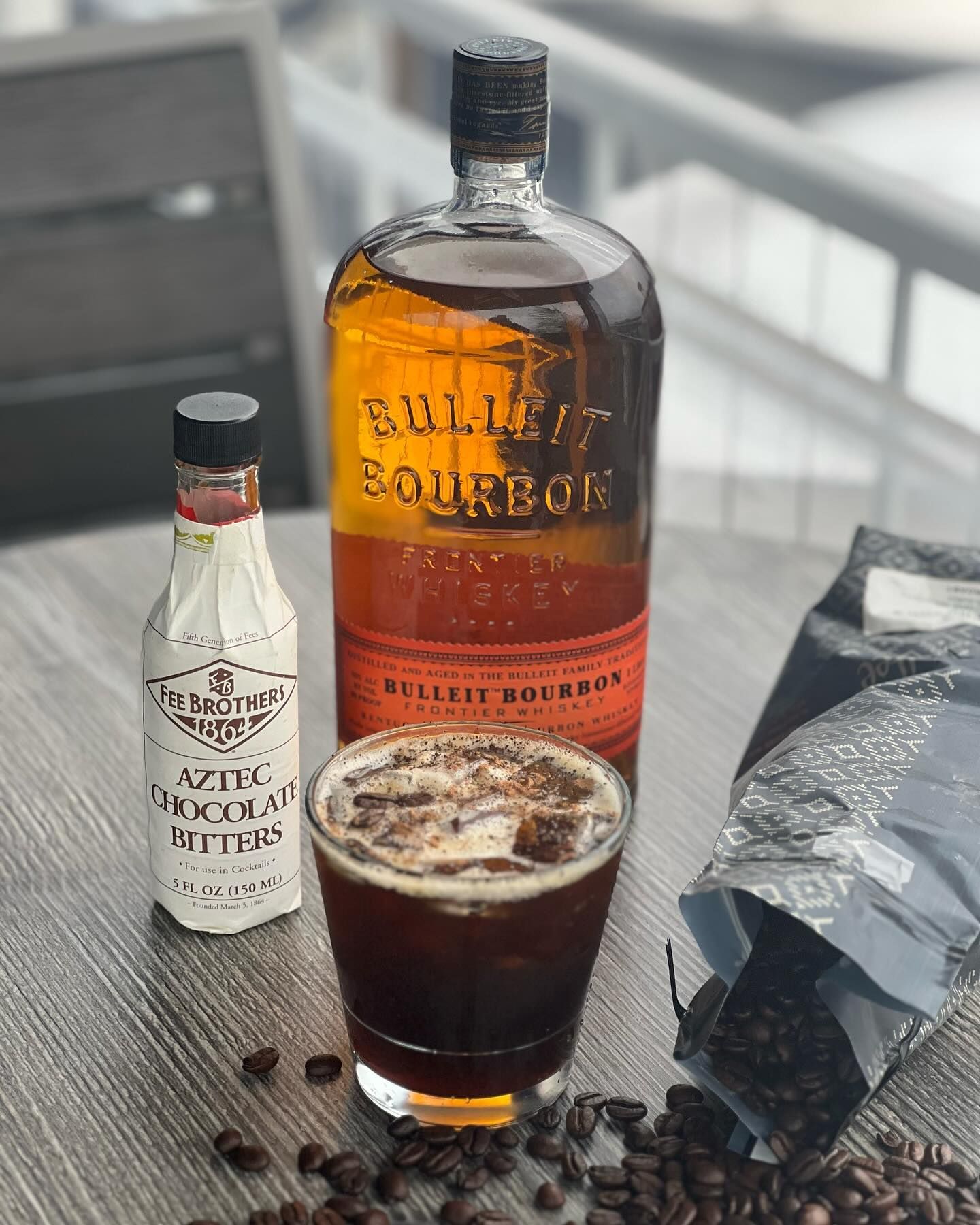 A cocktail with Bulleit Bourbon, Aztec Chocolate Bitters, coffee beans, and a bottle of bourbon.