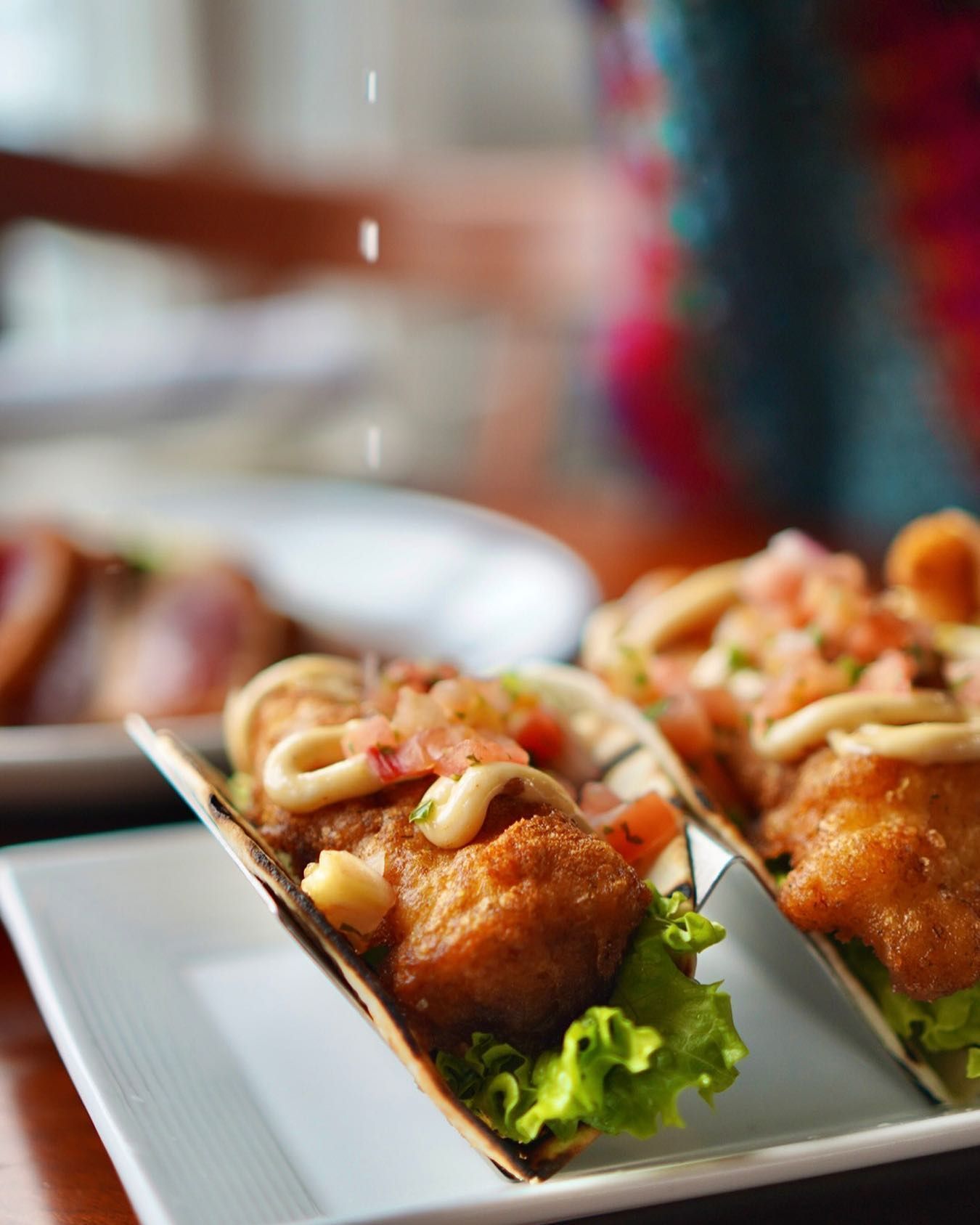 Close-up of two fish tacos topped with sauce and salsa, on a plate, with lettuce in the shells.