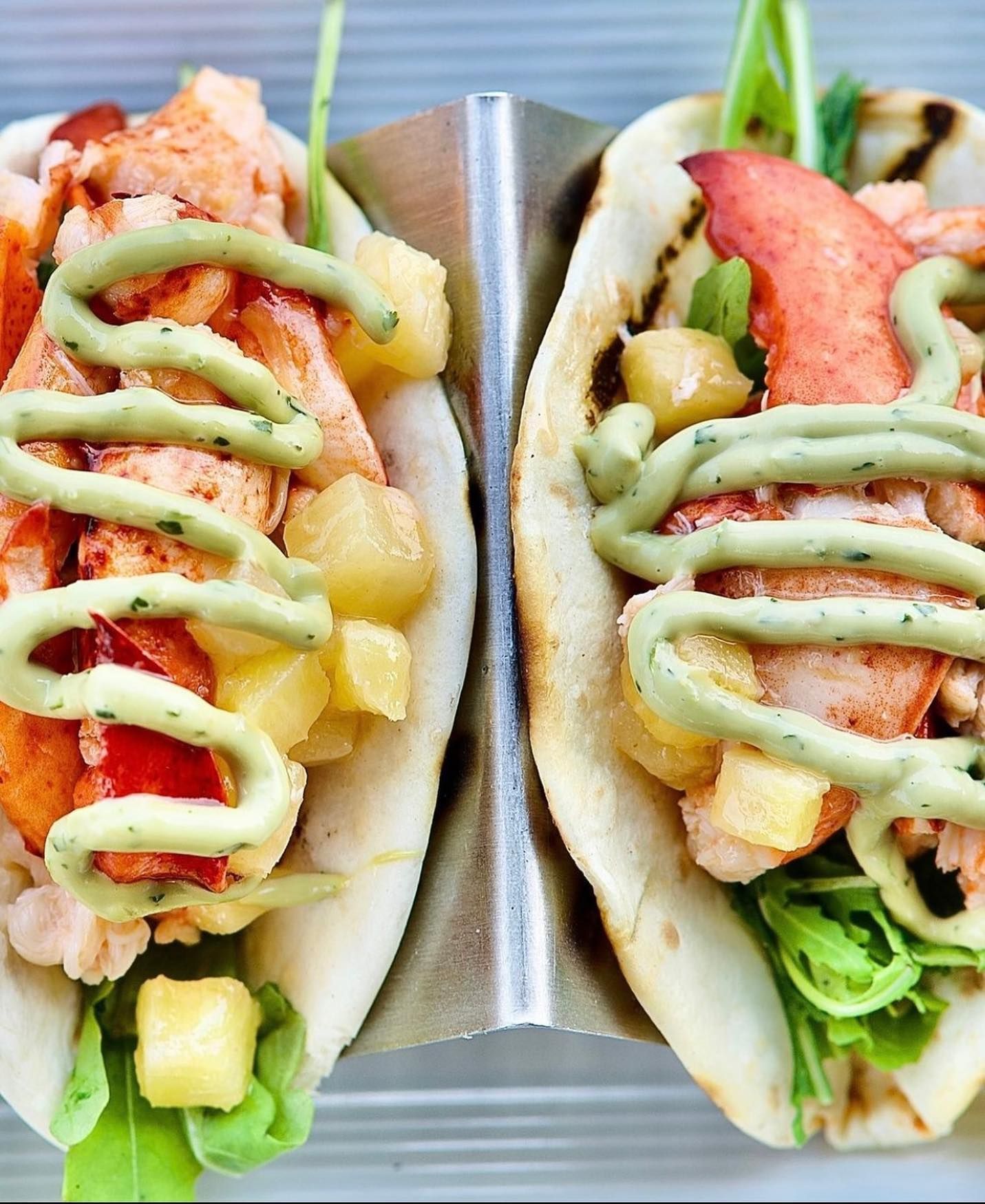 Lobster tacos with pineapple and green sauce, served in a metal holder.