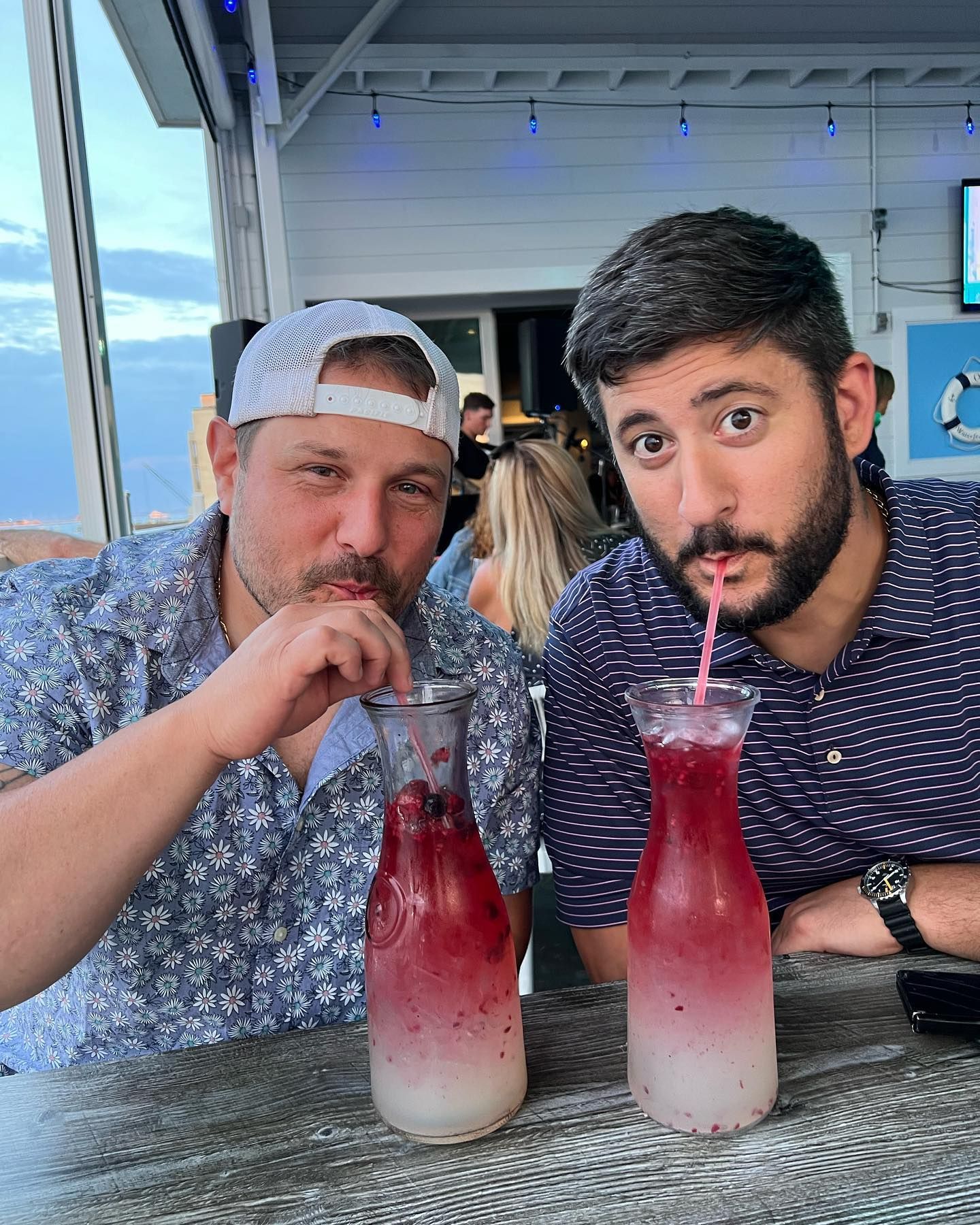 Two men drinking pink cocktails through straws outdoors.