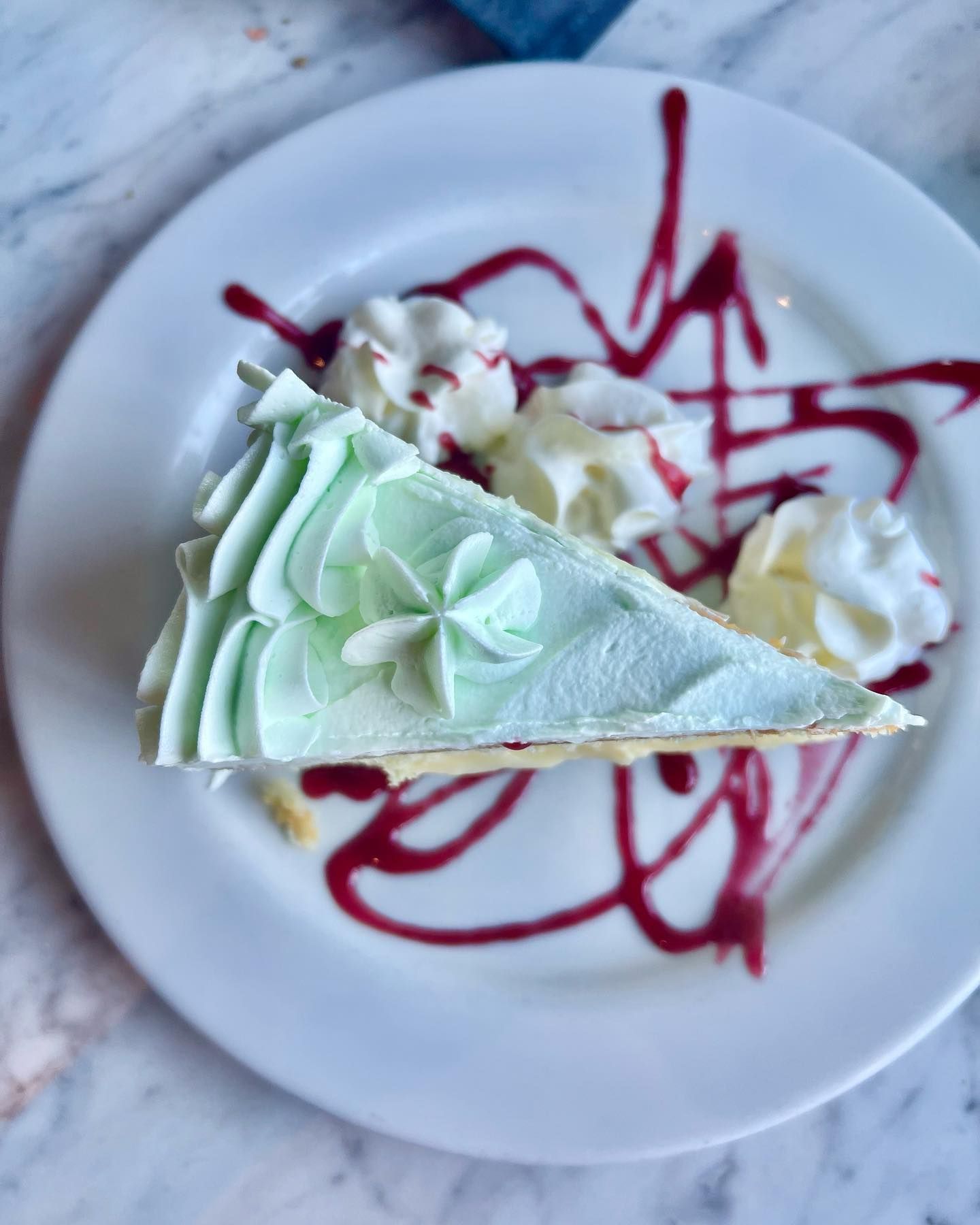 Slice of green frosted cake on a white plate with whipped cream and berry sauce.