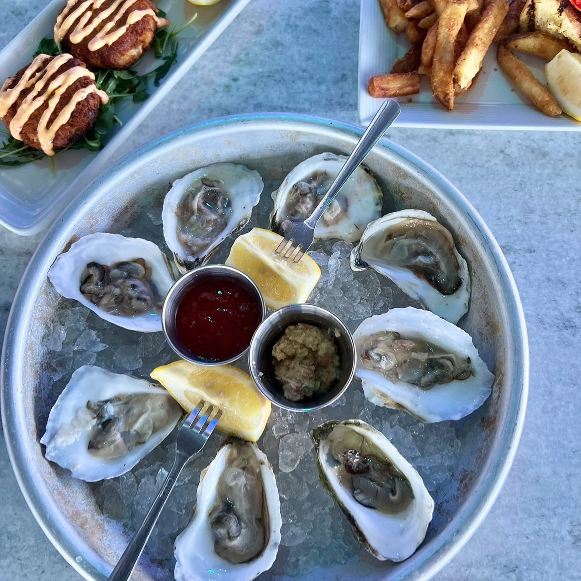 Oysters on ice with lemon wedges, cocktail sauce, and horseradish. Crab cakes and fries also visible.