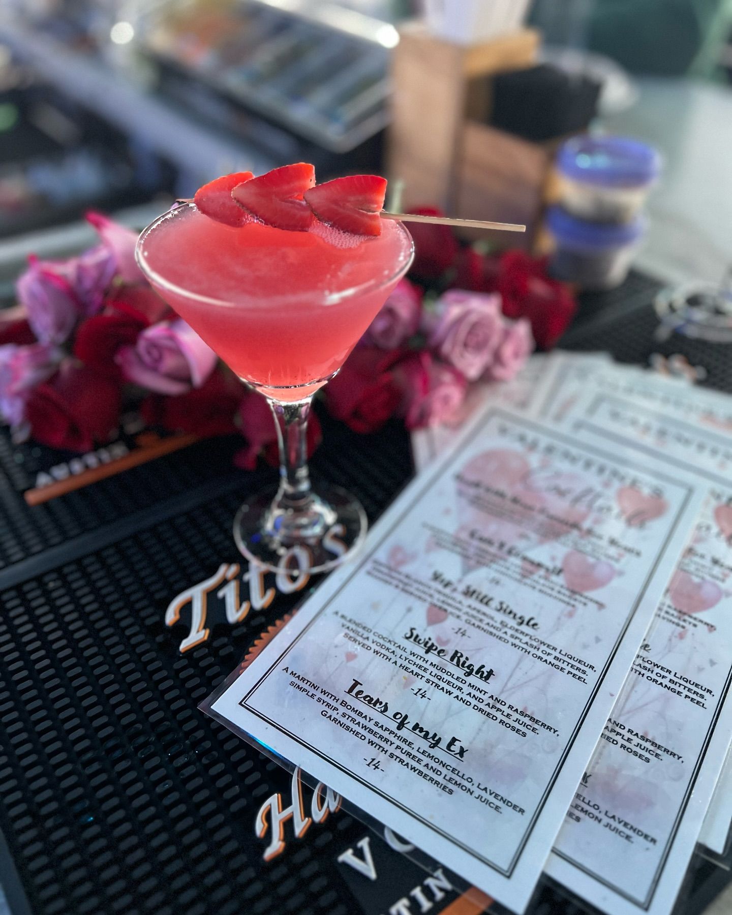 Cocktail in a martini glass with strawberry garnish; menu and flowers in the background.