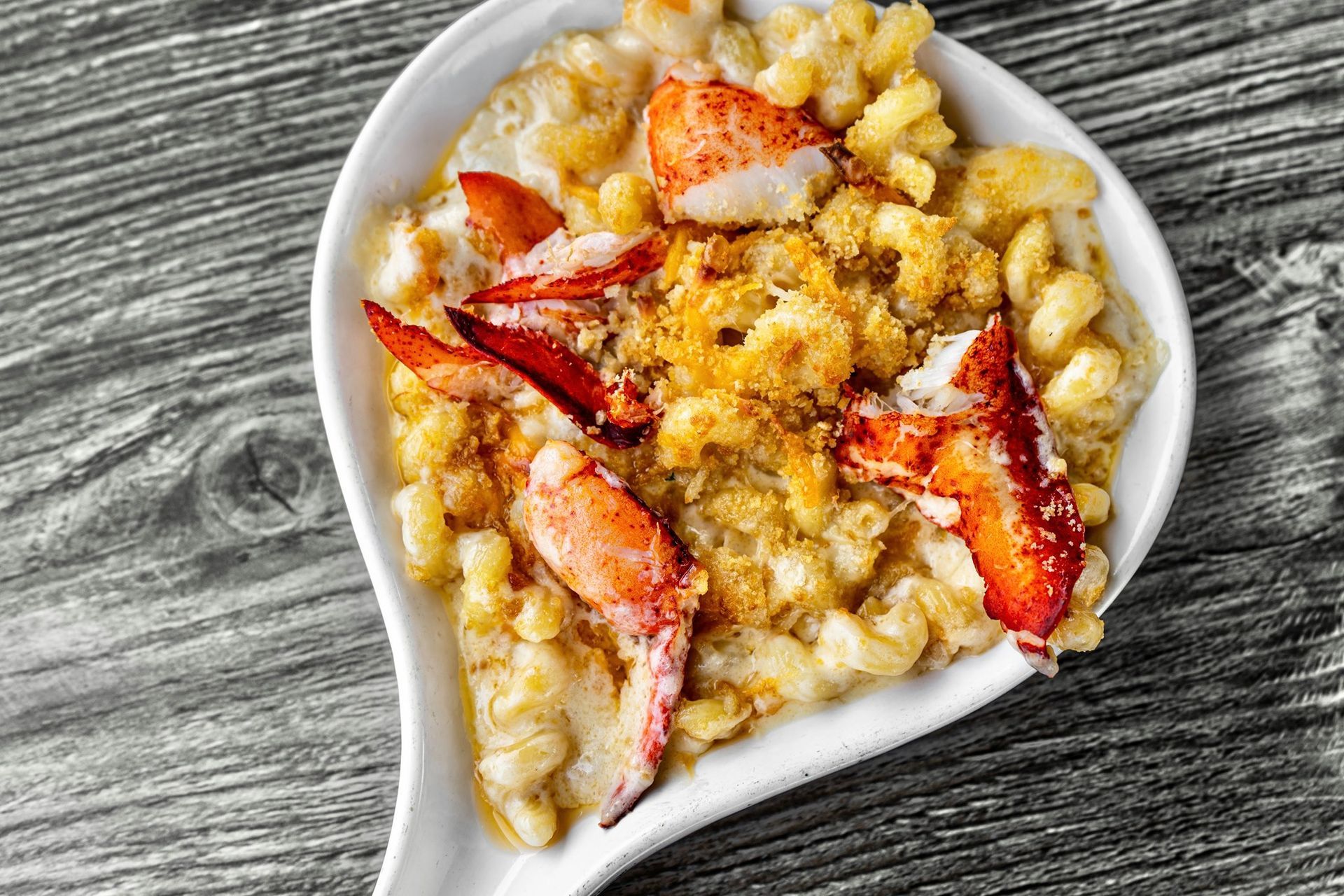 Lobster mac and cheese in a white dish on a wood grain background.