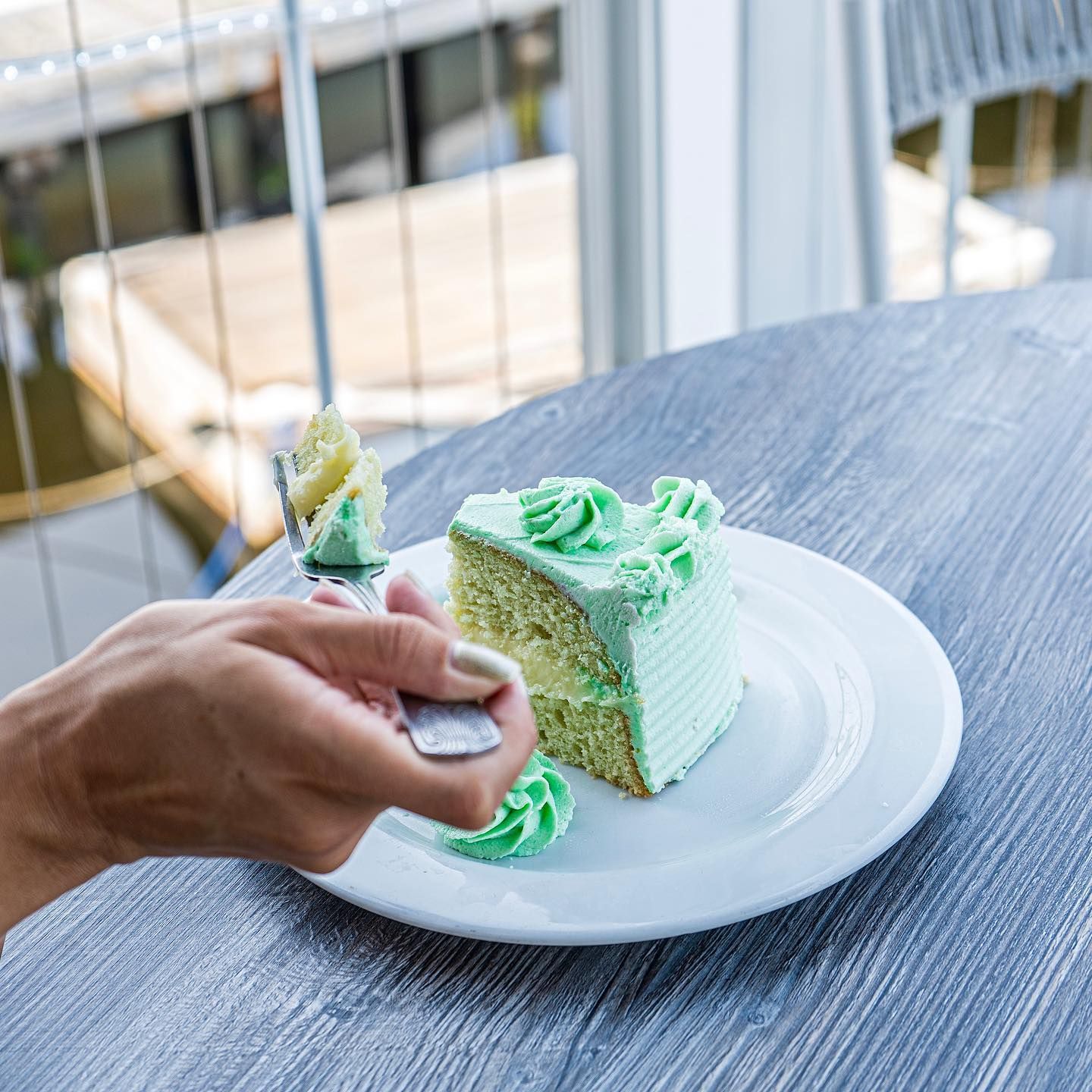 Hand holding fork cutting into slice of green frosted cake on a white plate.