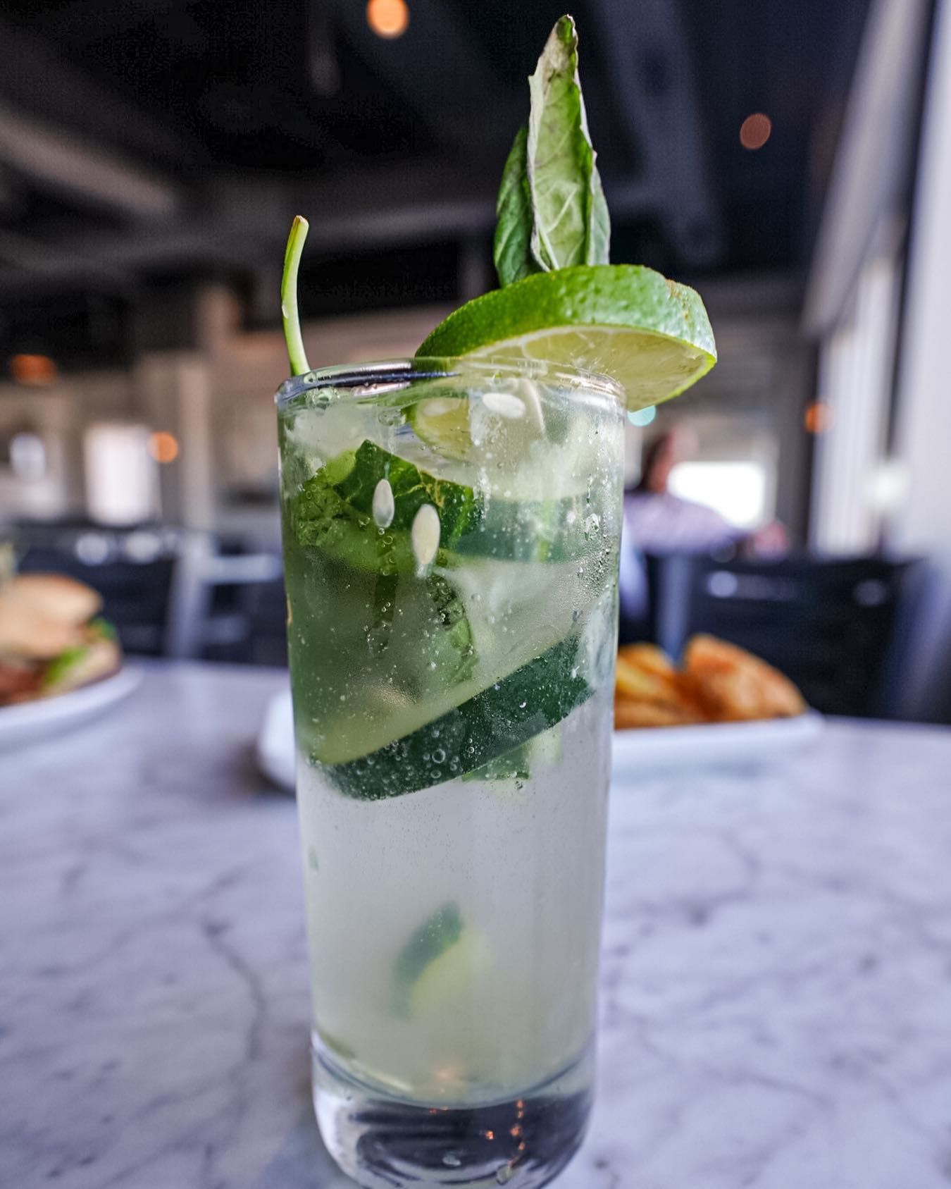 Cocktail with lime and mint in tall glass, on marble table, restaurant setting.