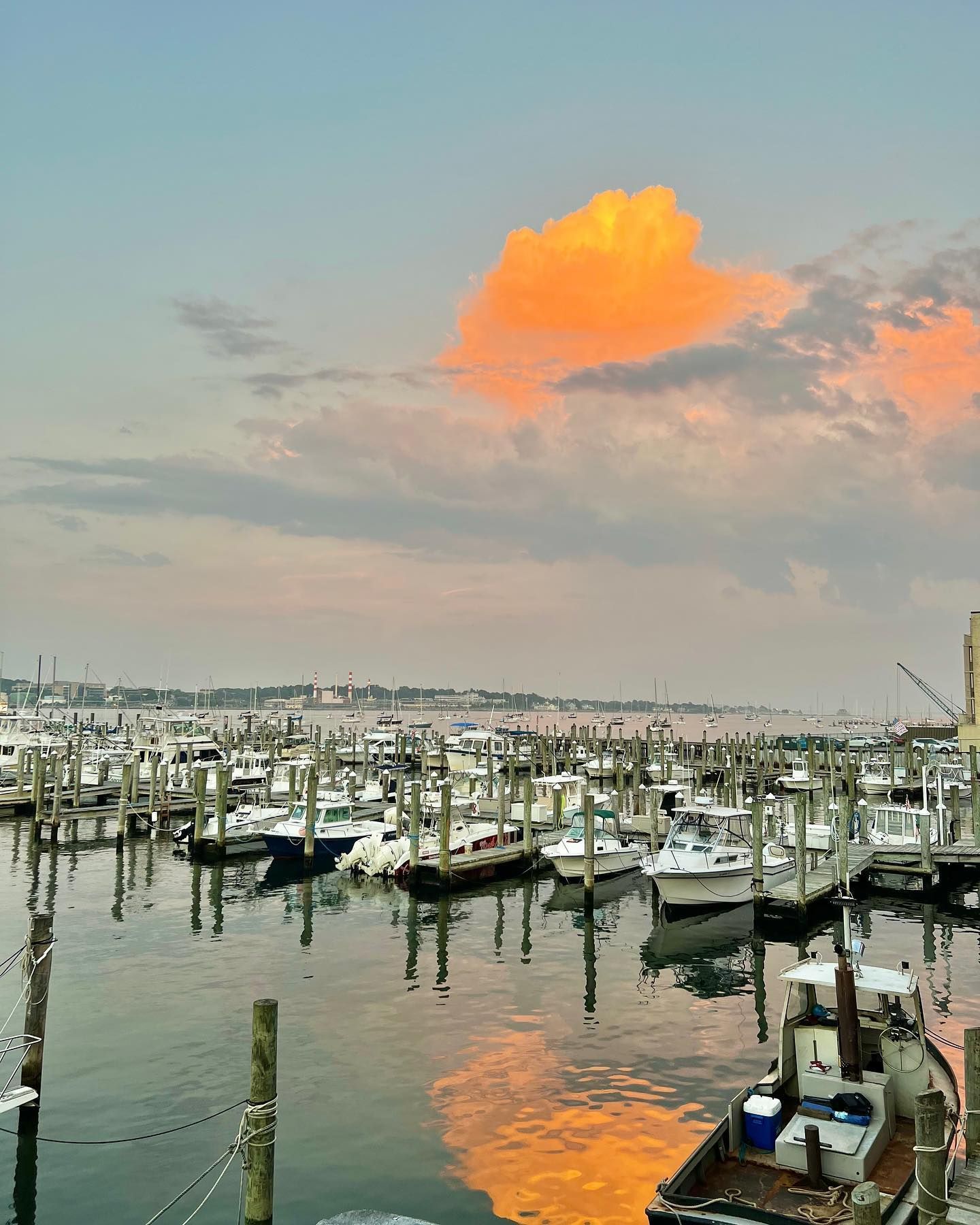 Boats docked in a harbor at dusk, with an orange-tinged cloud reflecting in the water.