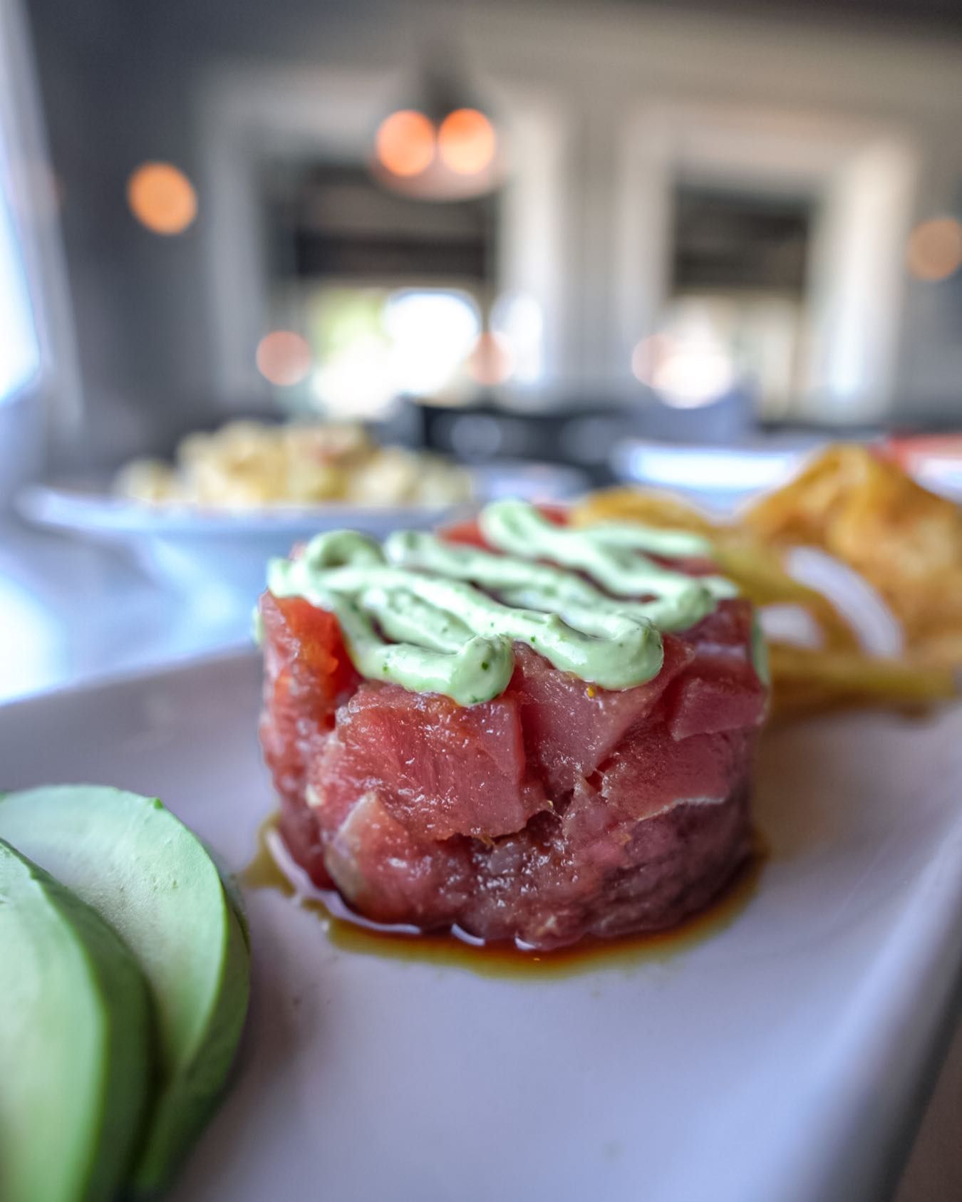 Tuna tartare topped with green sauce, served with avocado slices and chips.