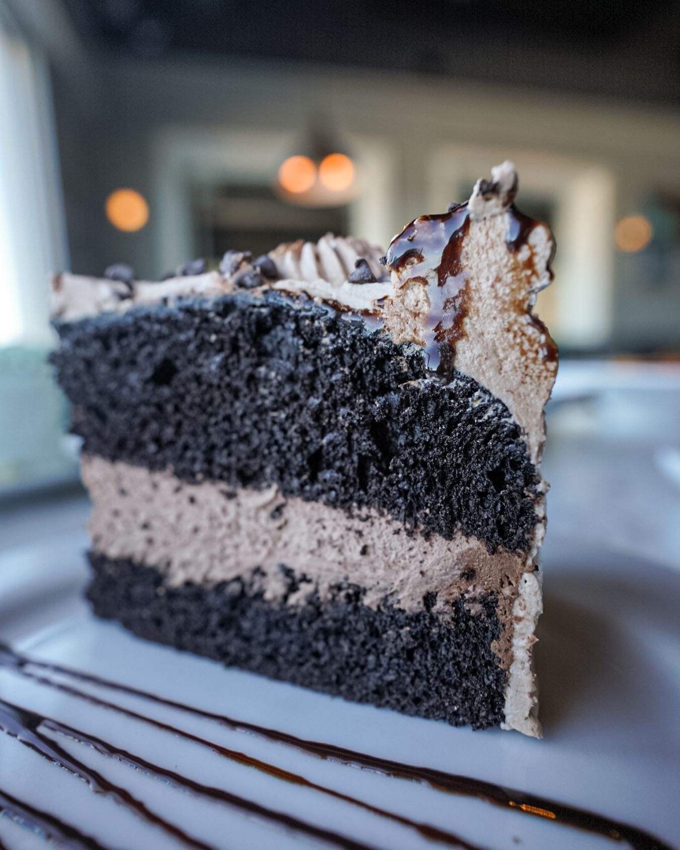 Slice of dark chocolate cake with chocolate frosting, on white plate.