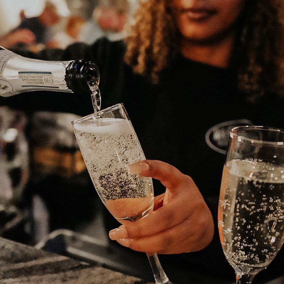 Bartender pouring sparkling wine into a glass; another full glass sits next to it.
