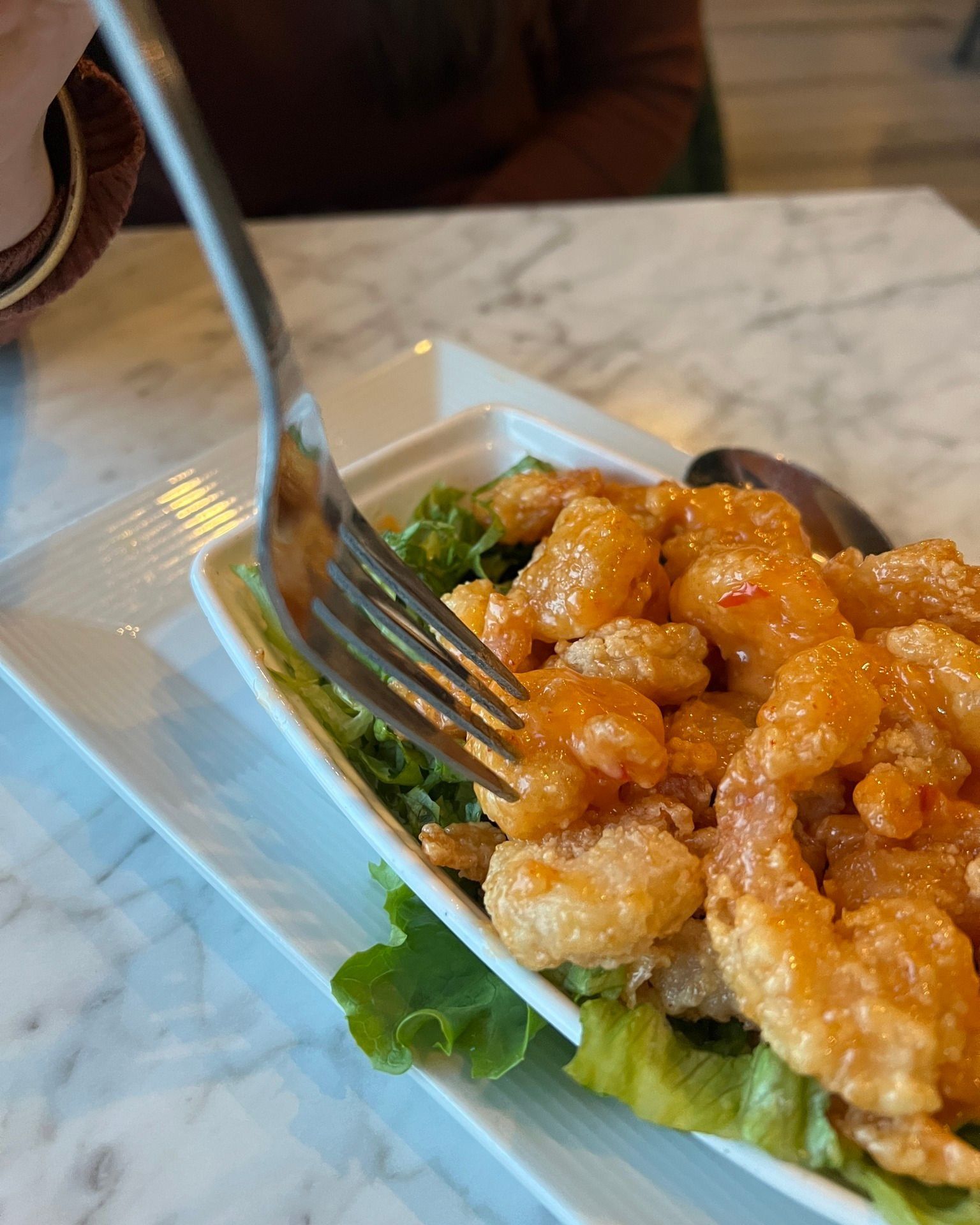Shrimp dish with sauce, on a bed of lettuce, being eaten with a fork.