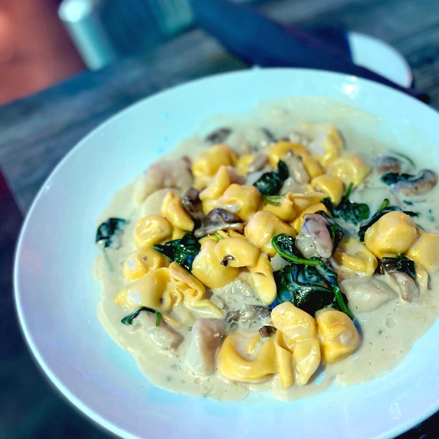 Tortellini pasta with spinach and mushrooms in creamy sauce on a white plate.