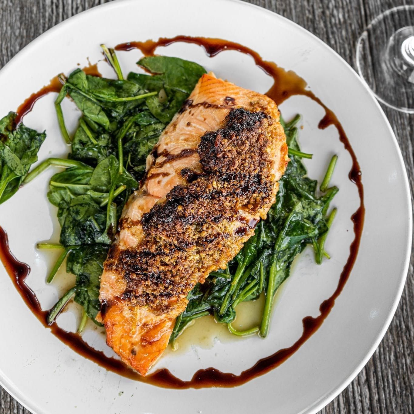 Grilled salmon over spinach, drizzled with balsamic glaze on a white plate.