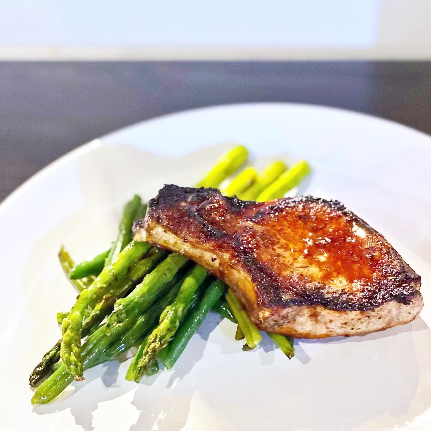 Grilled pork chop with asparagus on a white plate.