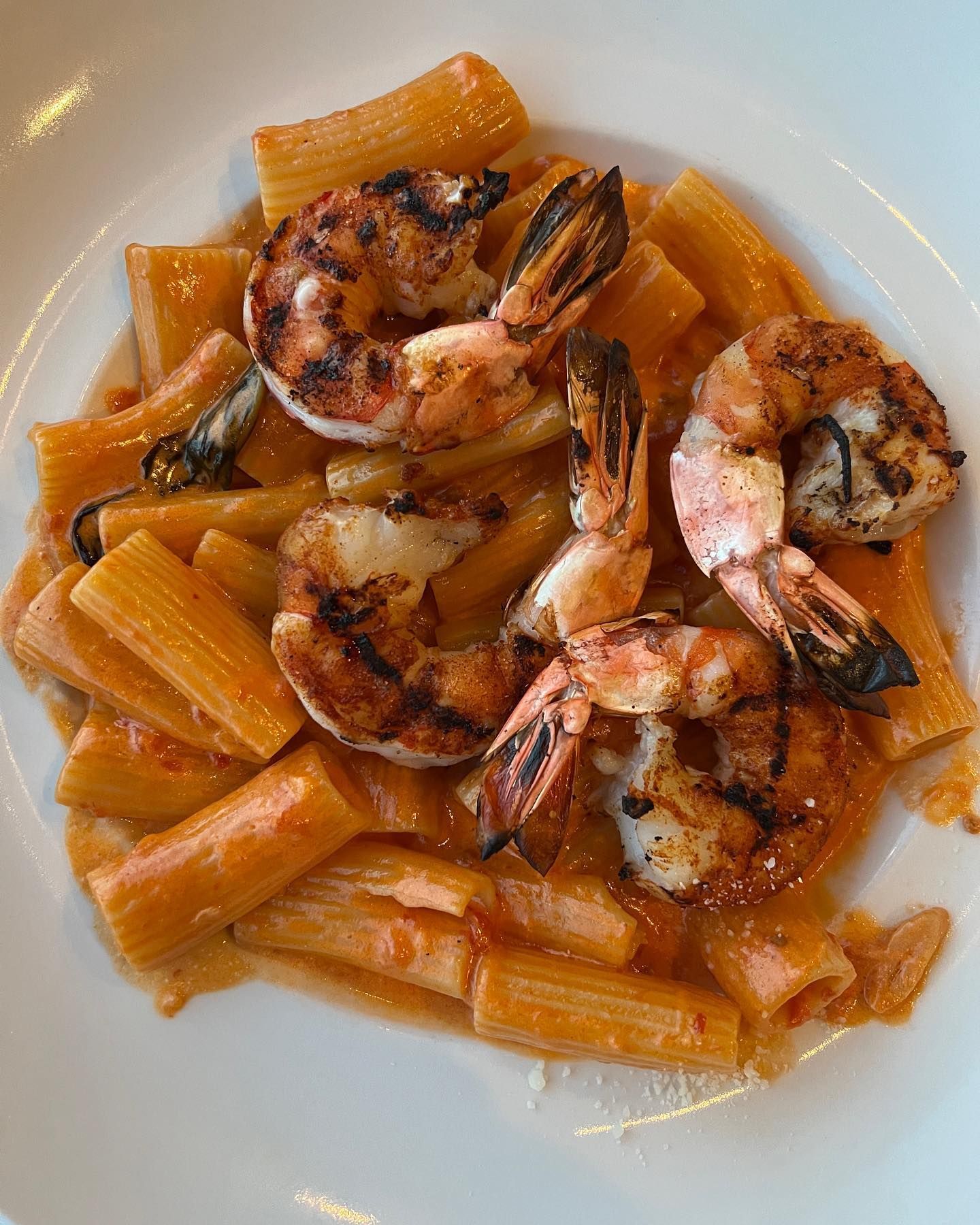 Rigatoni pasta with grilled shrimp in a creamy tomato sauce on a white plate.