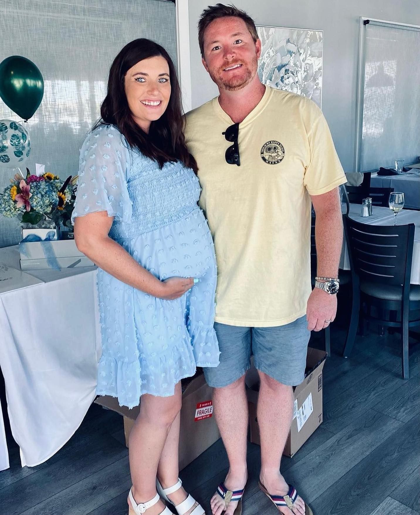 Pregnant woman in blue dress and man in yellow shirt pose together, baby shower setting.