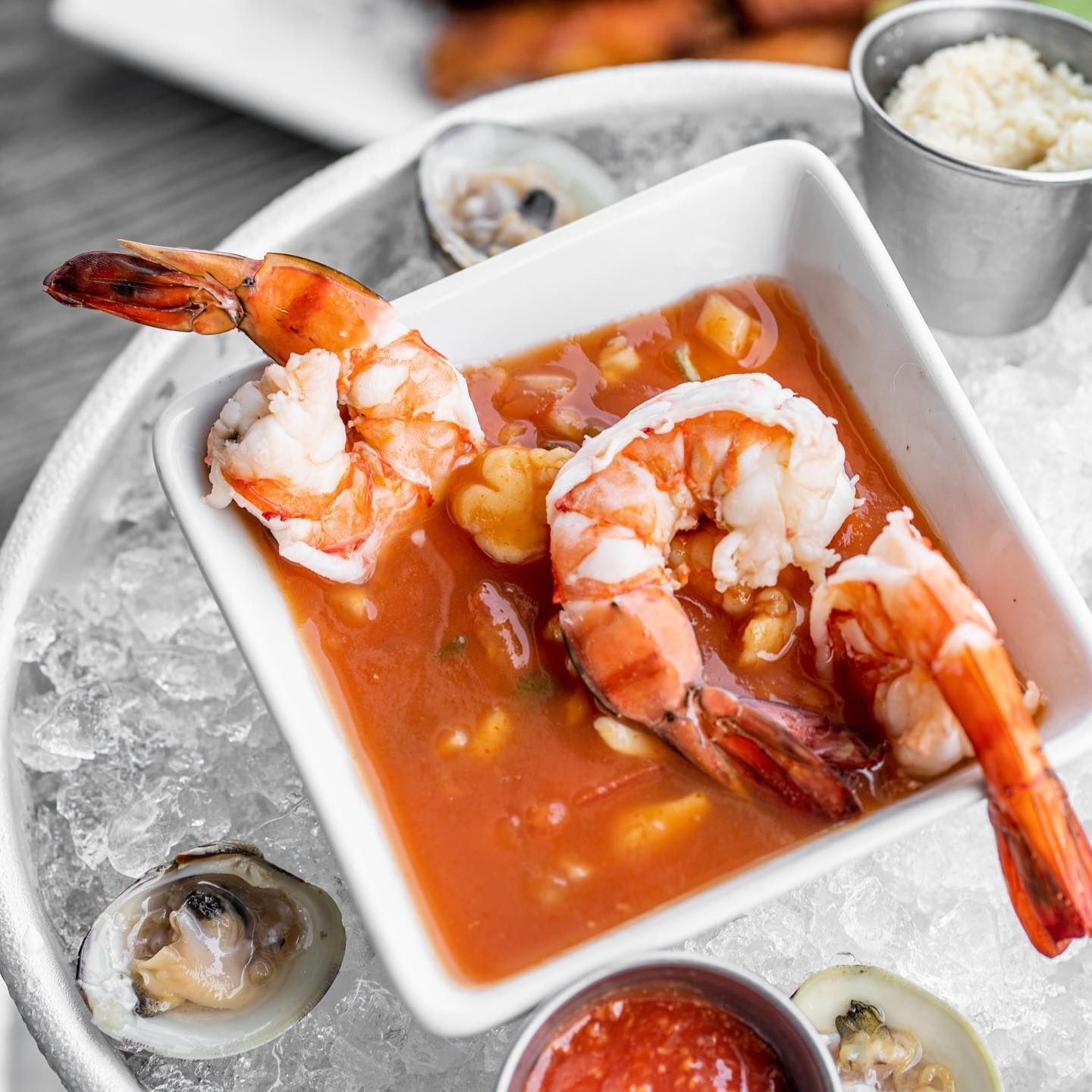 Shrimp cocktail in a white bowl, served on ice, with clams and sauce.