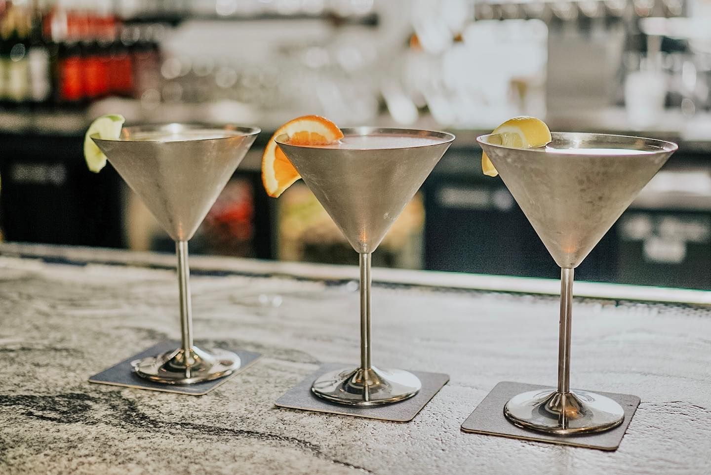 Three martini cocktails with citrus garnishes on a bar.