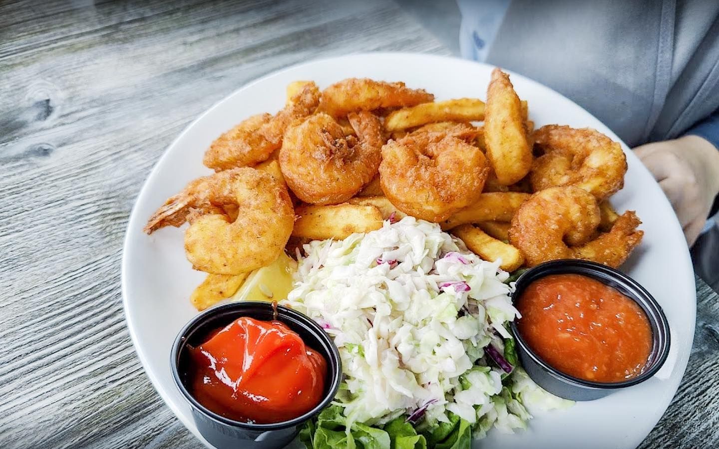 Plate of fried shrimp, fries, coleslaw, and dipping sauces.