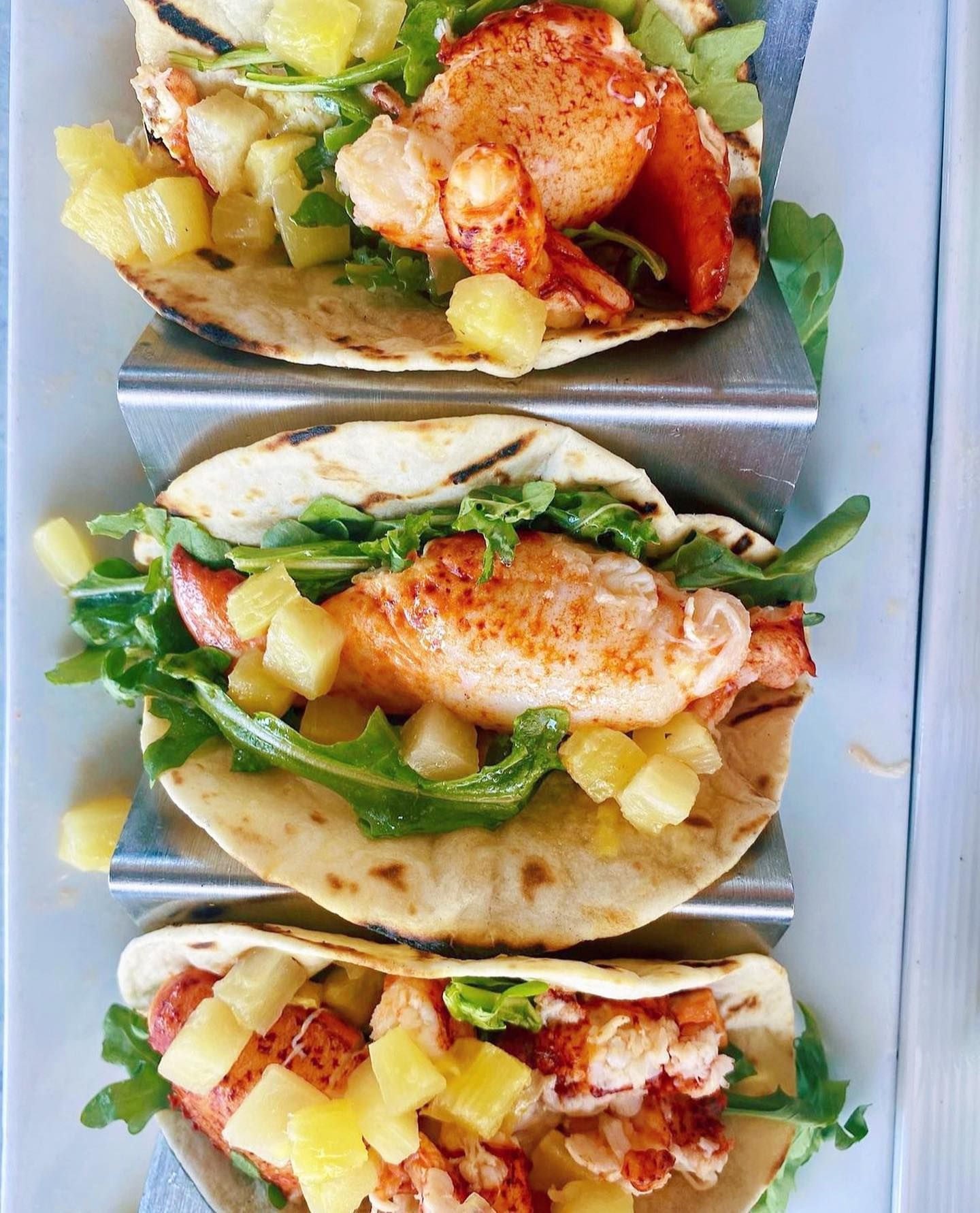 Lobster tacos with pineapple and arugula, served in a metal taco holder.