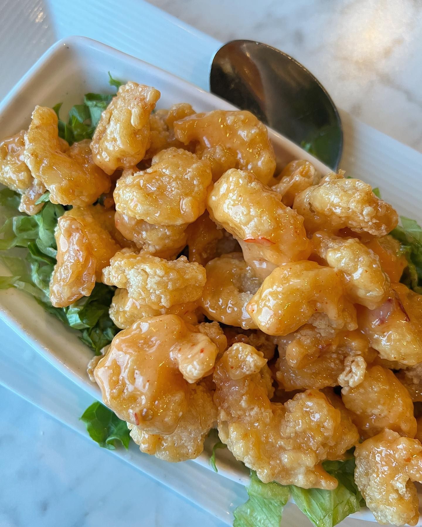 Fried shrimp with a creamy orange sauce, served on lettuce in a white rectangular dish.