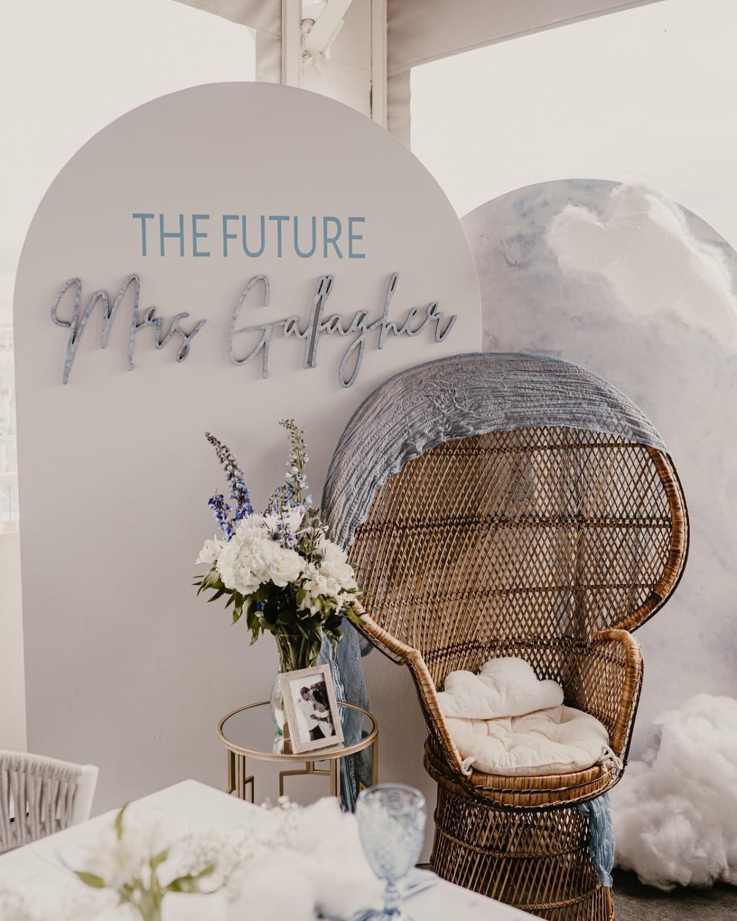 Decorated event backdrop with The Future Mrs. Gallagher in blue on white, featuring a peacock chair and flower arrangement.