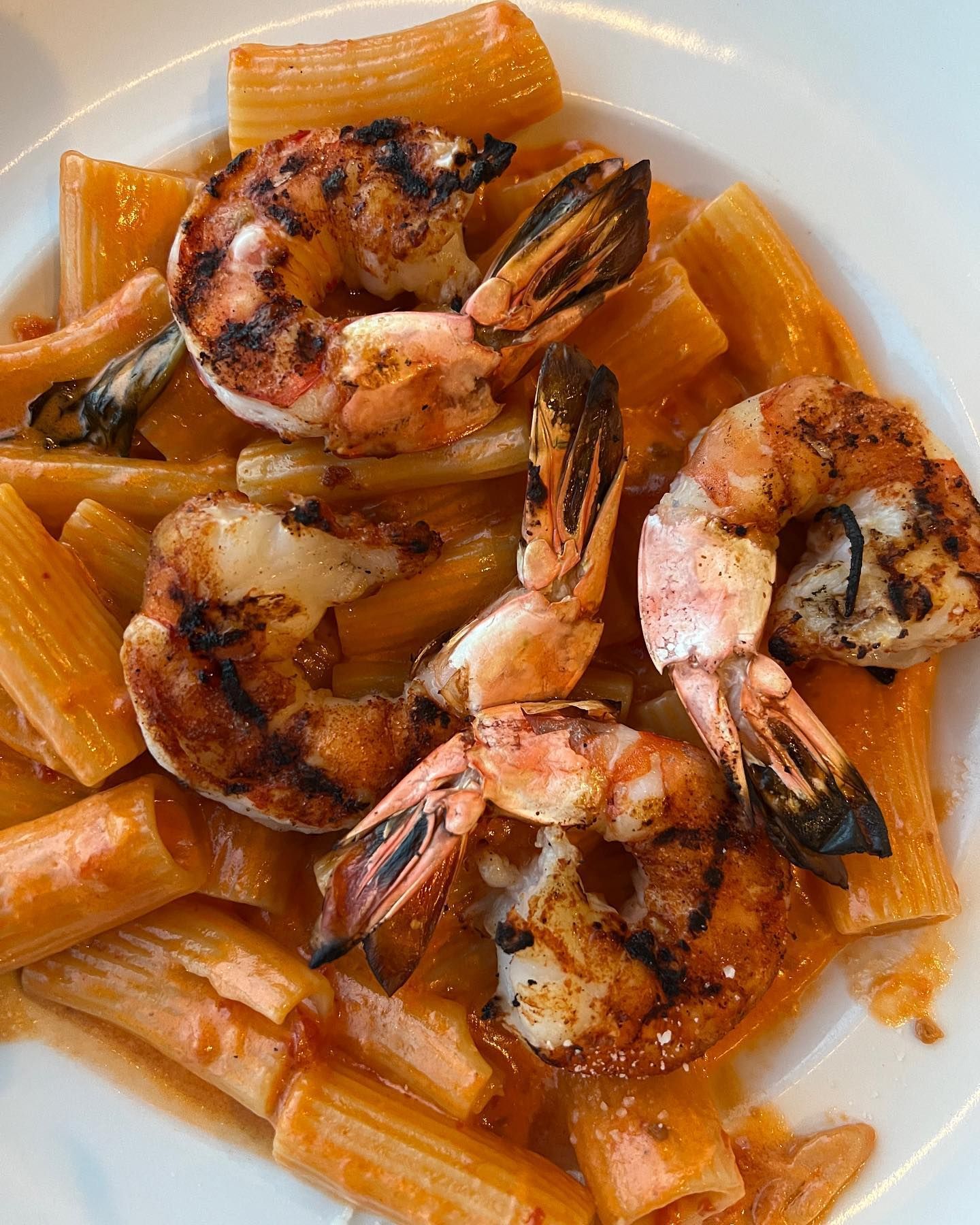 Pasta dish with grilled shrimp in a red sauce, on a white plate.