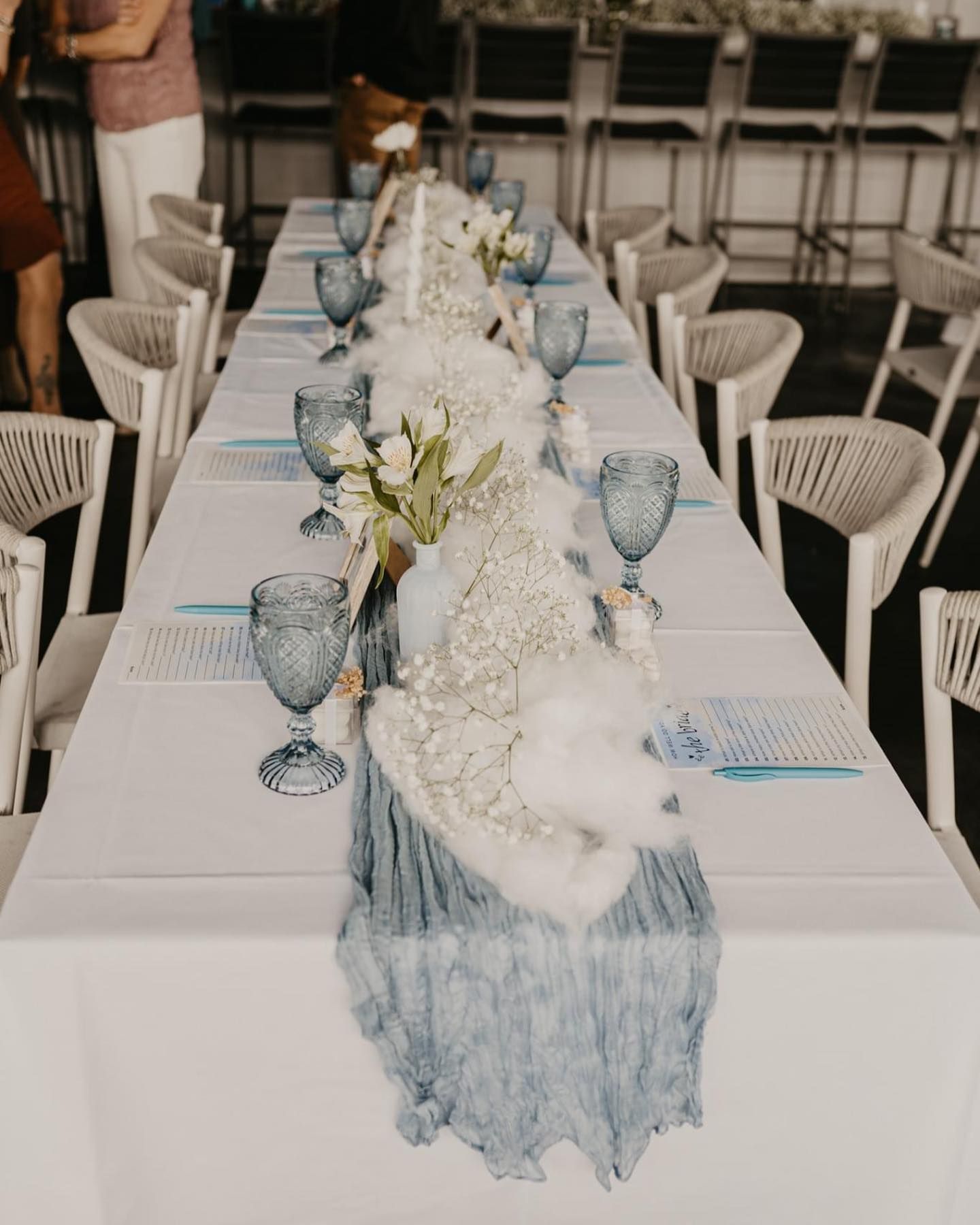 Long table set for a formal event, with blue accents and white chairs.