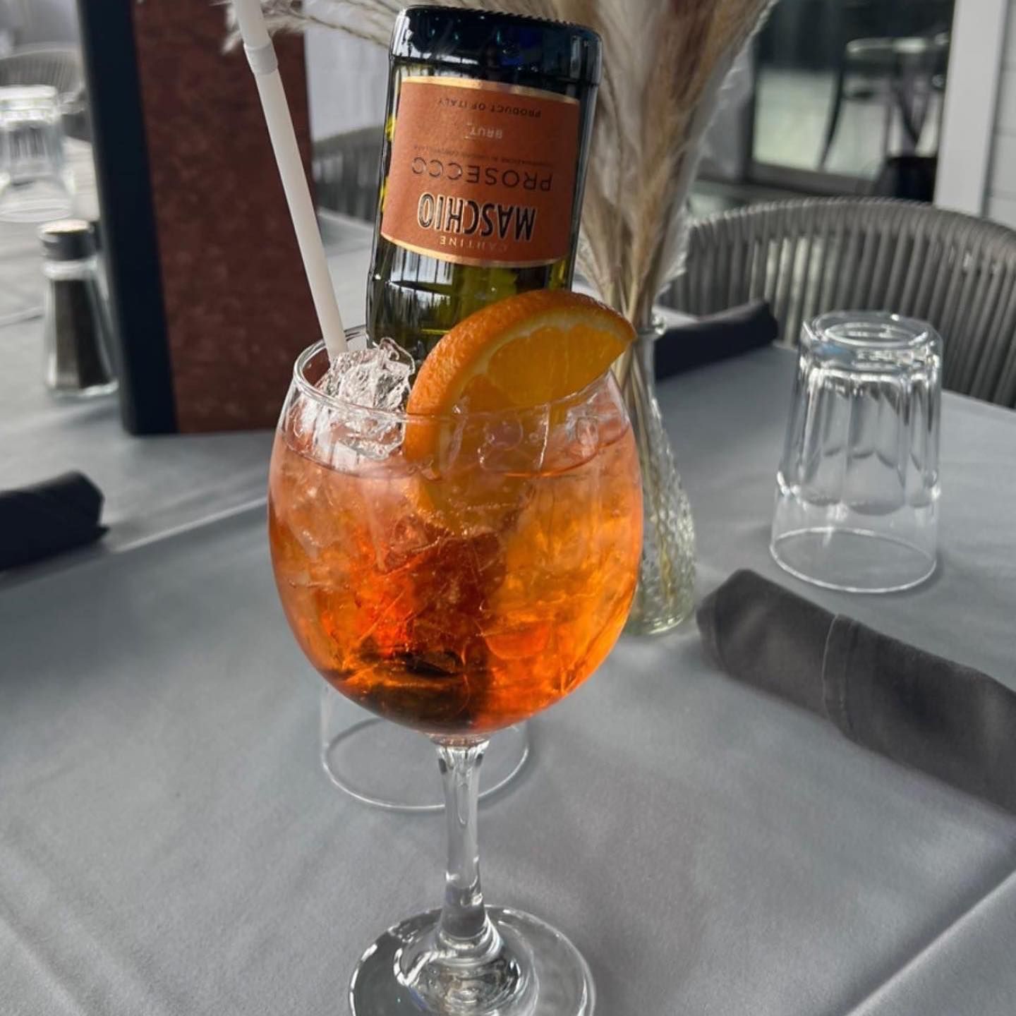 Aperol spritz with orange slice and Prosecco bottle on a restaurant table.