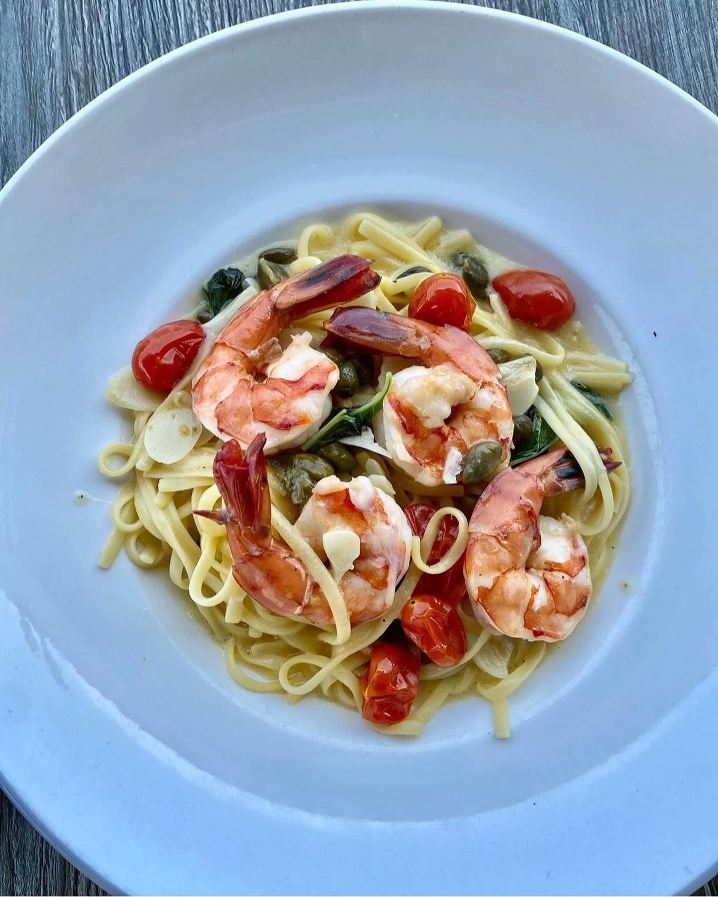 Shrimp scampi pasta with cherry tomatoes and capers in a white bowl.