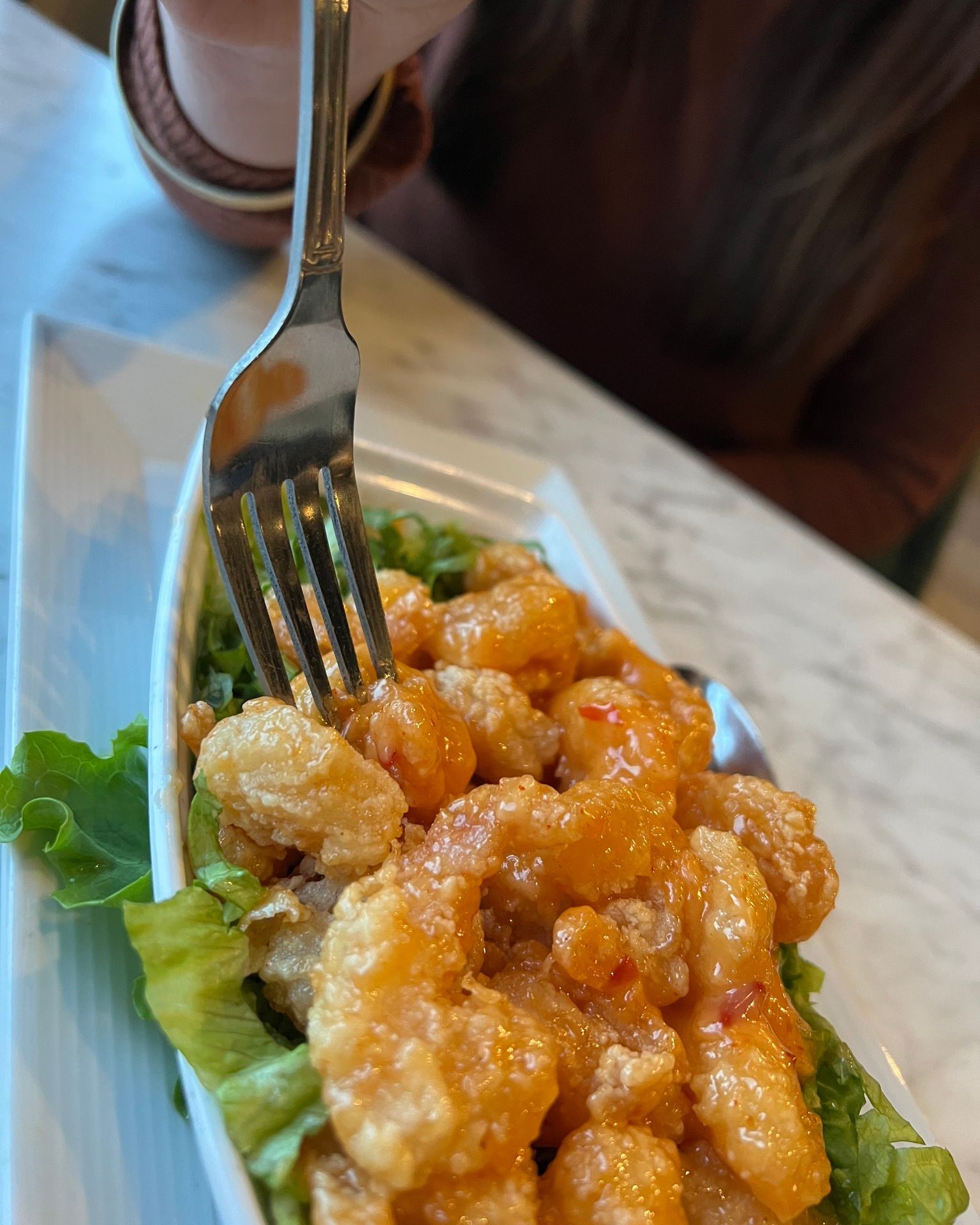 Person using a fork to eat crispy, orange-sauced shrimp on a bed of lettuce.