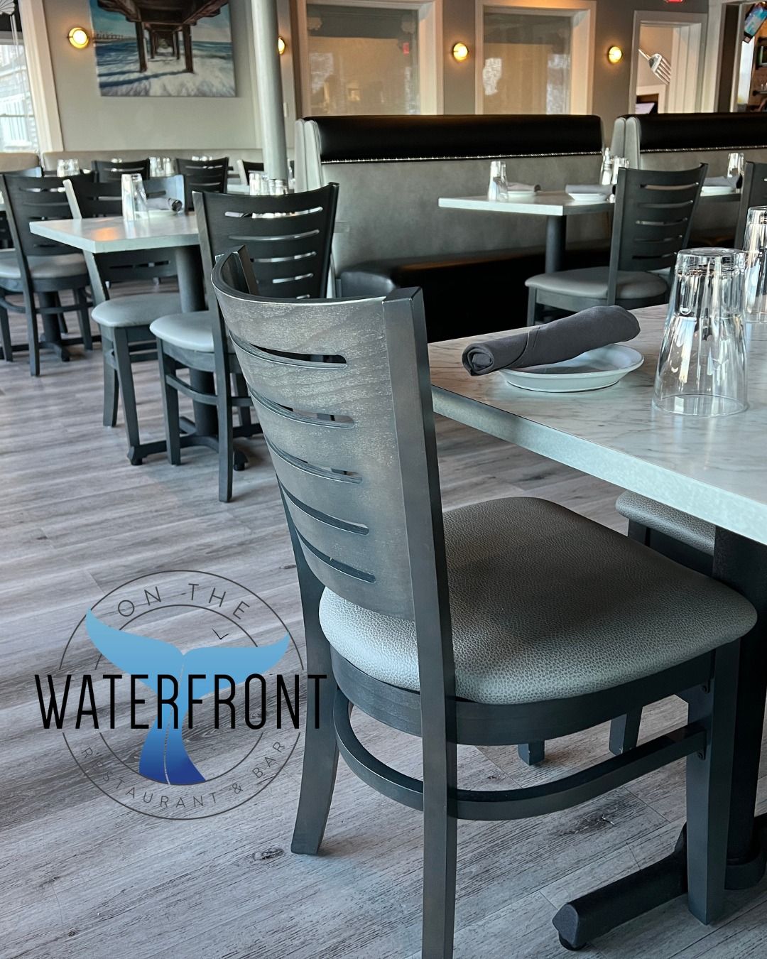 Restaurant dining room with tables, chairs, and place settings. Gray color scheme with wood and upholstered furniture.