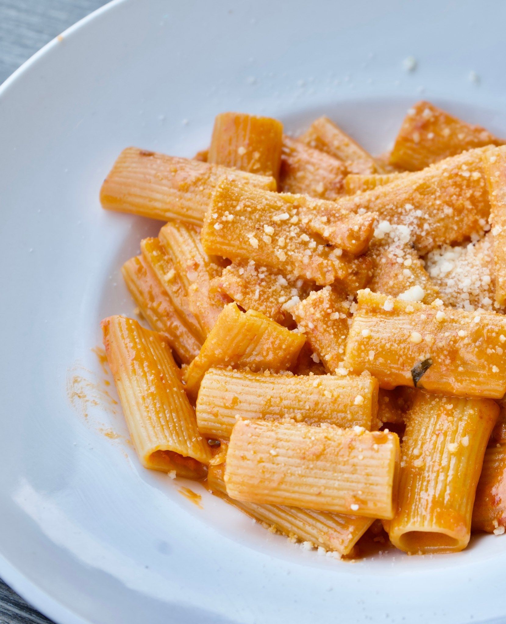 Rigatoni pasta with creamy orange sauce, topped with grated cheese, in a white bowl.