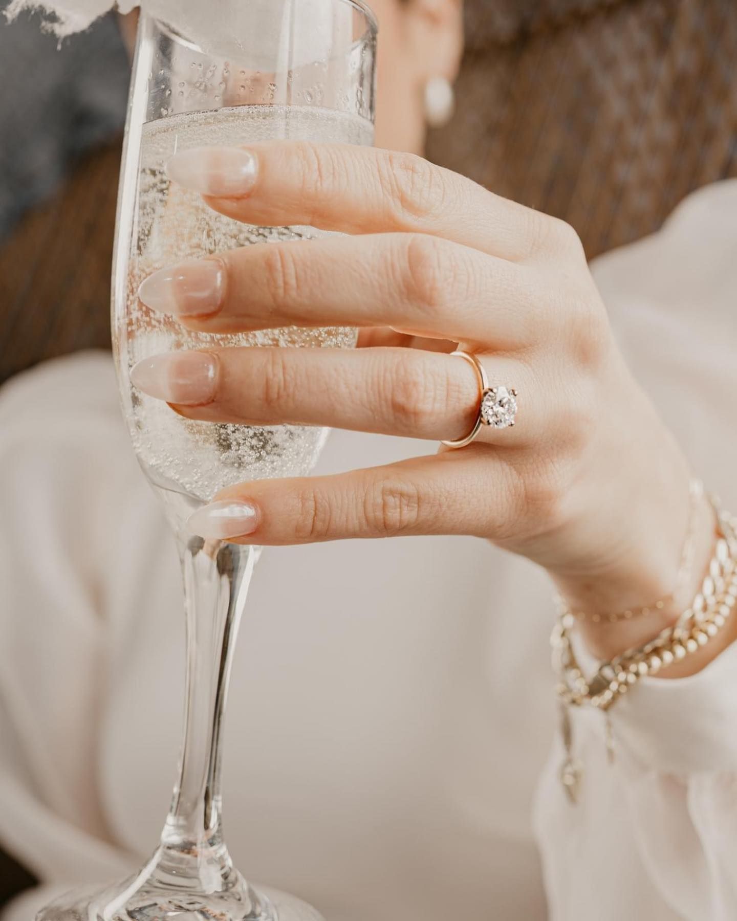 Hand holding a champagne flute, wearing an engagement ring and bracelet.