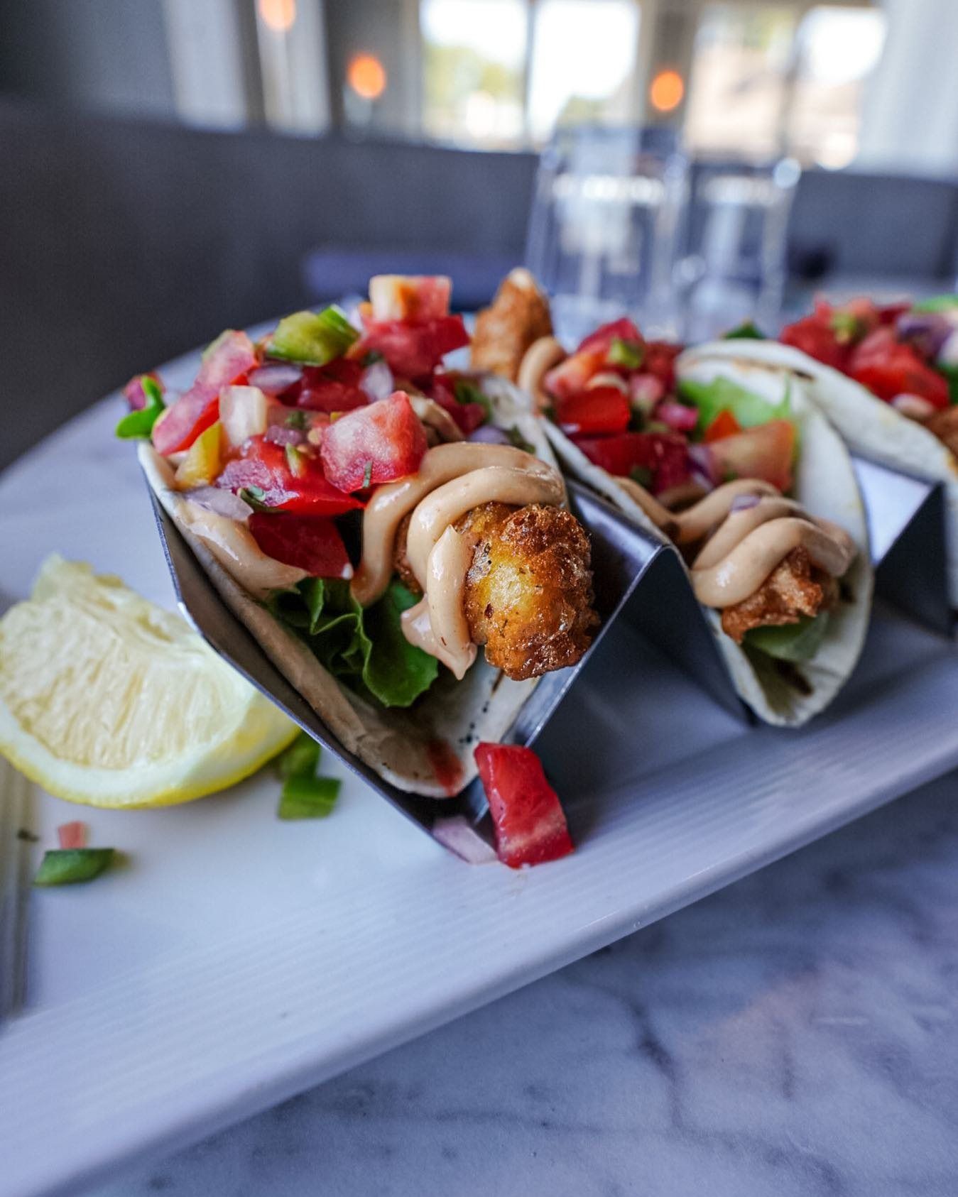 Tacos with fried filling, strawberry salsa, and sauce on a white plate with lemon.
