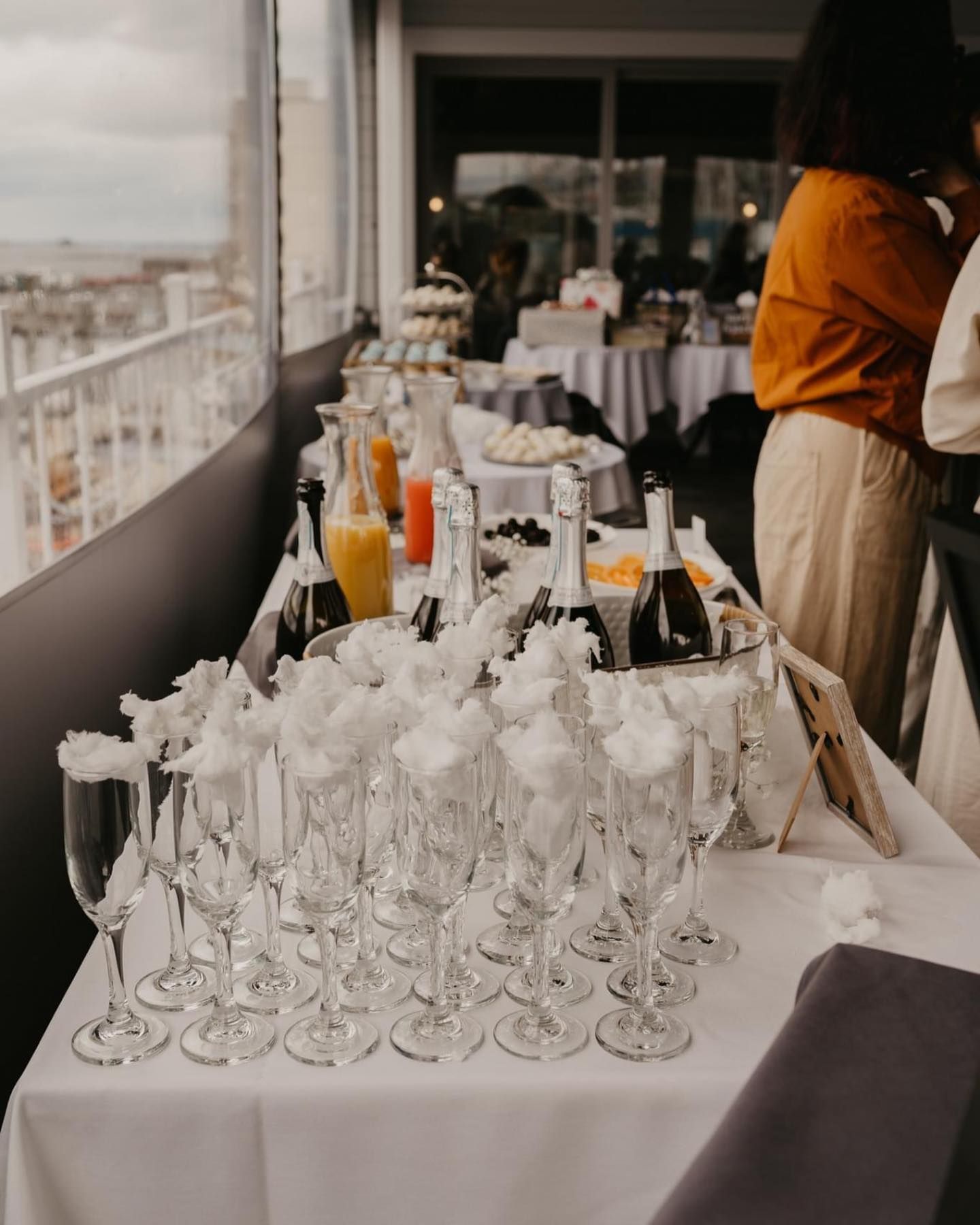 A table with champagne flutes, bottles, and food at an event overlooking a cityscape.