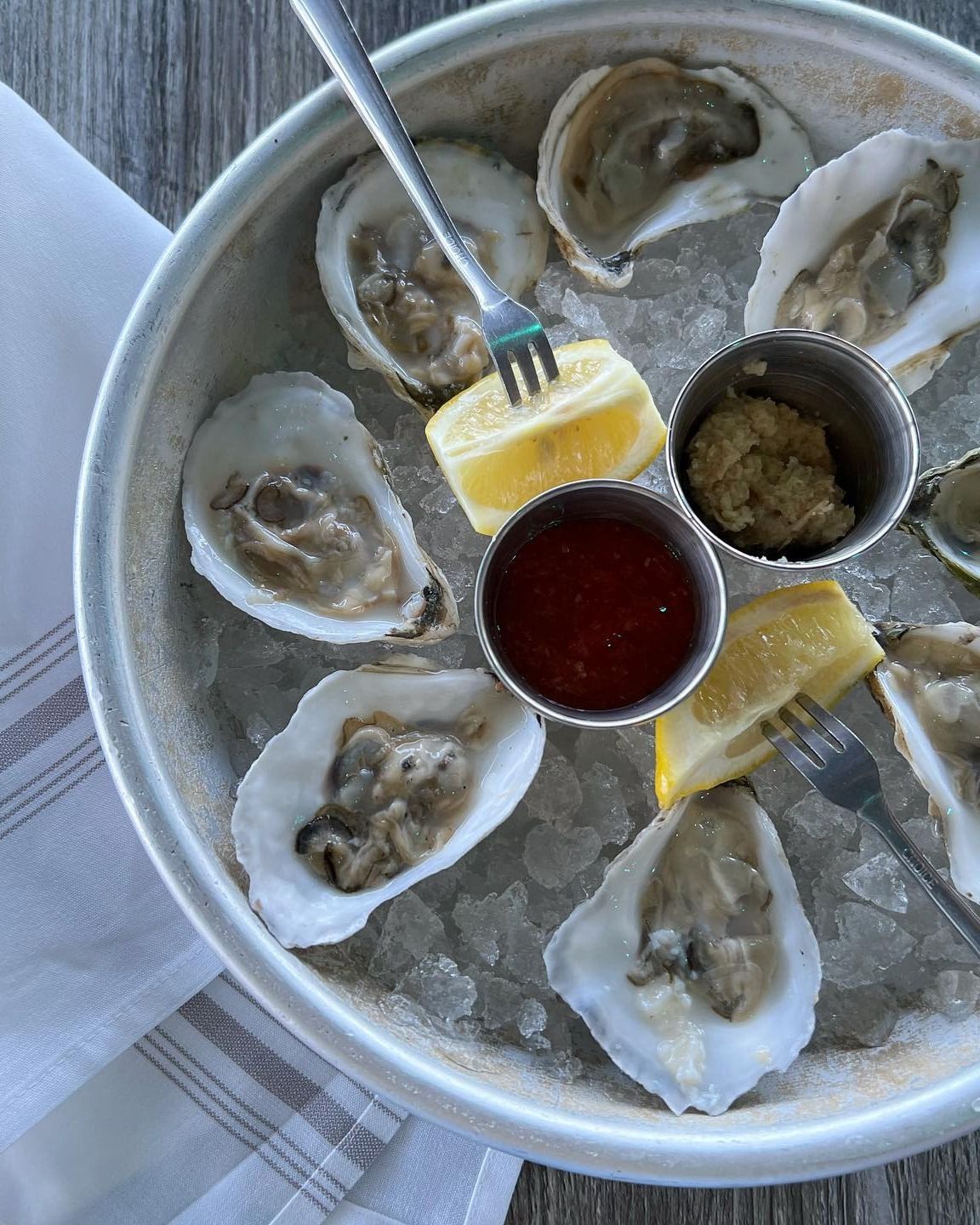 Plate of oysters on ice with cocktail sauce, horseradish, lemon wedges, and forks.