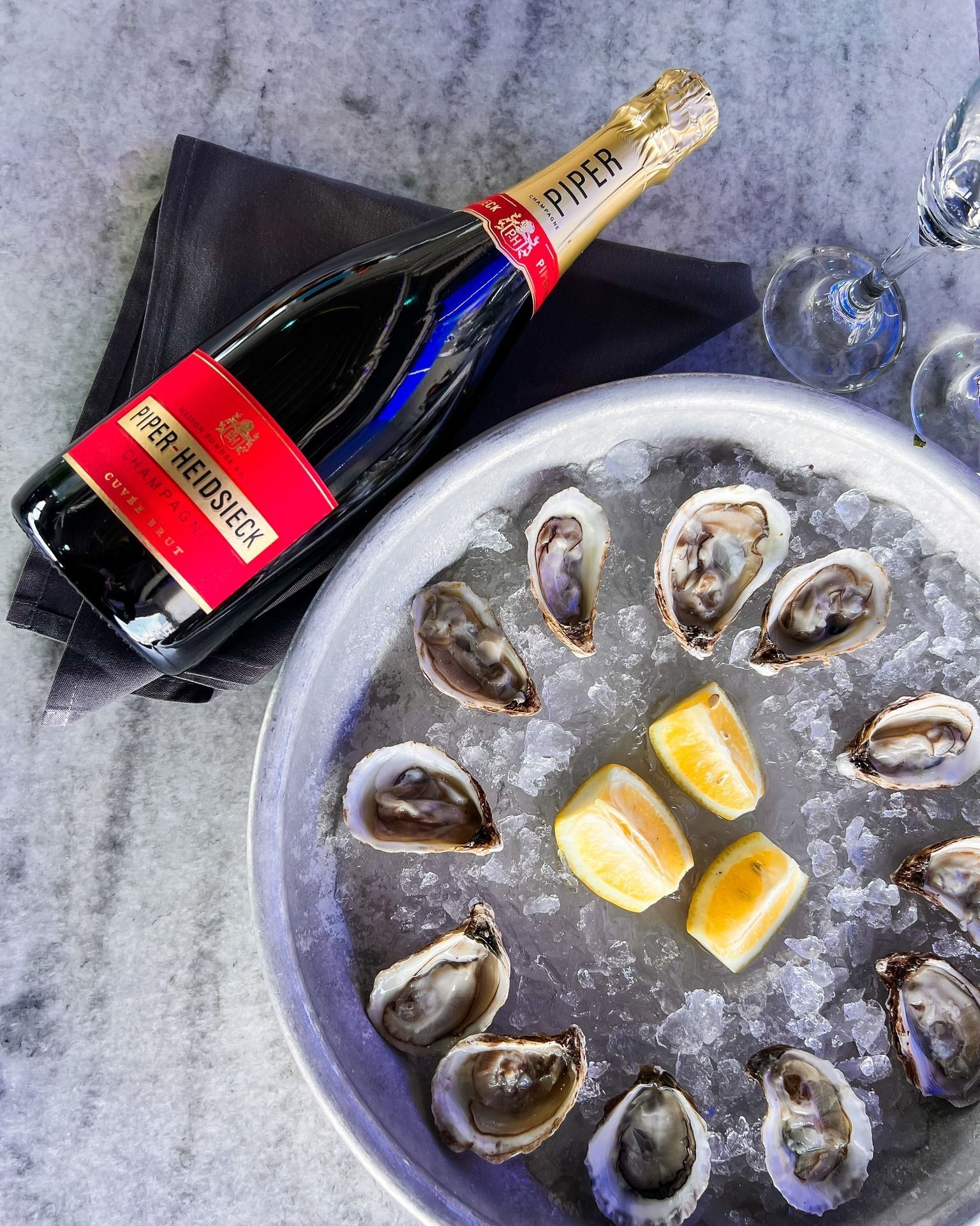 Champagne bottle and oyster platter with lemon wedges on a gray surface.