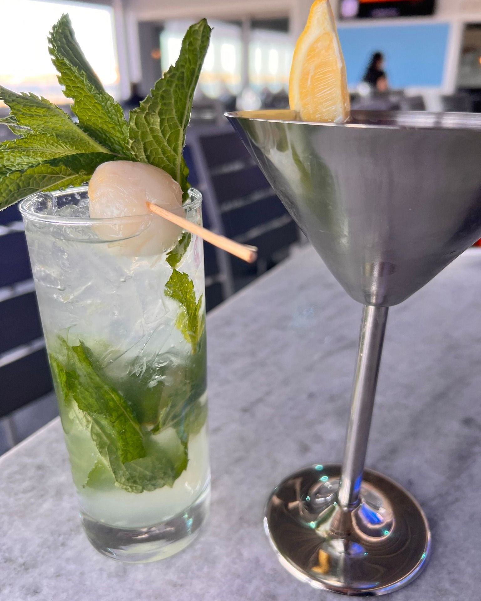 Mojito with lychee and martini with lemon slice on a table.