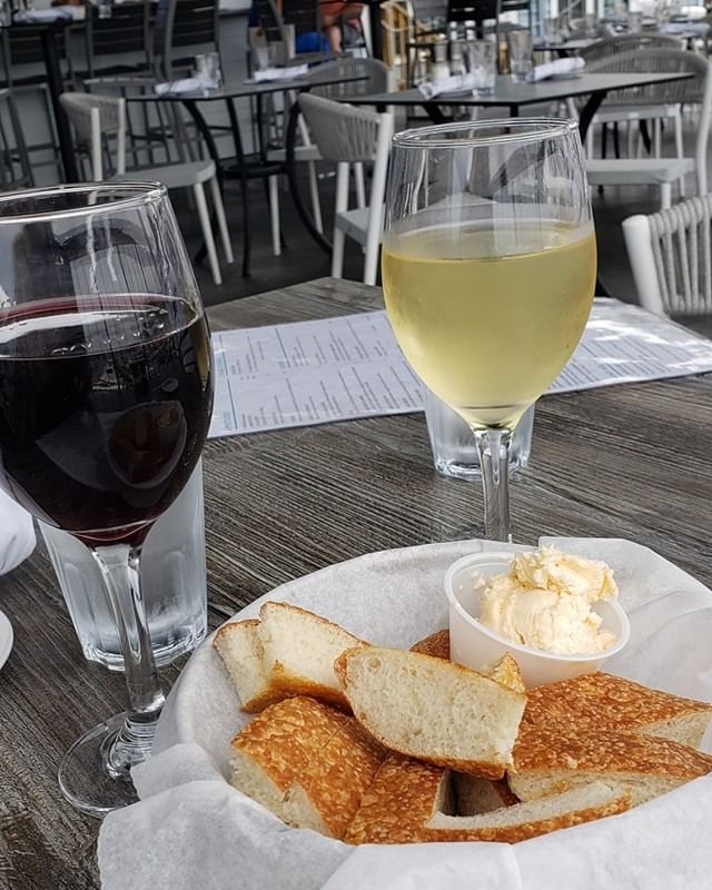 Red and white wine glasses, bread basket, and butter on a table at an outdoor restaurant.
