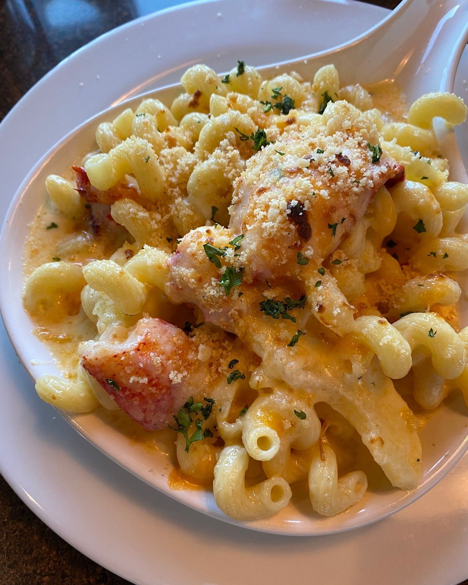 Lobster mac and cheese in a white bowl, topped with breadcrumbs and parsley.