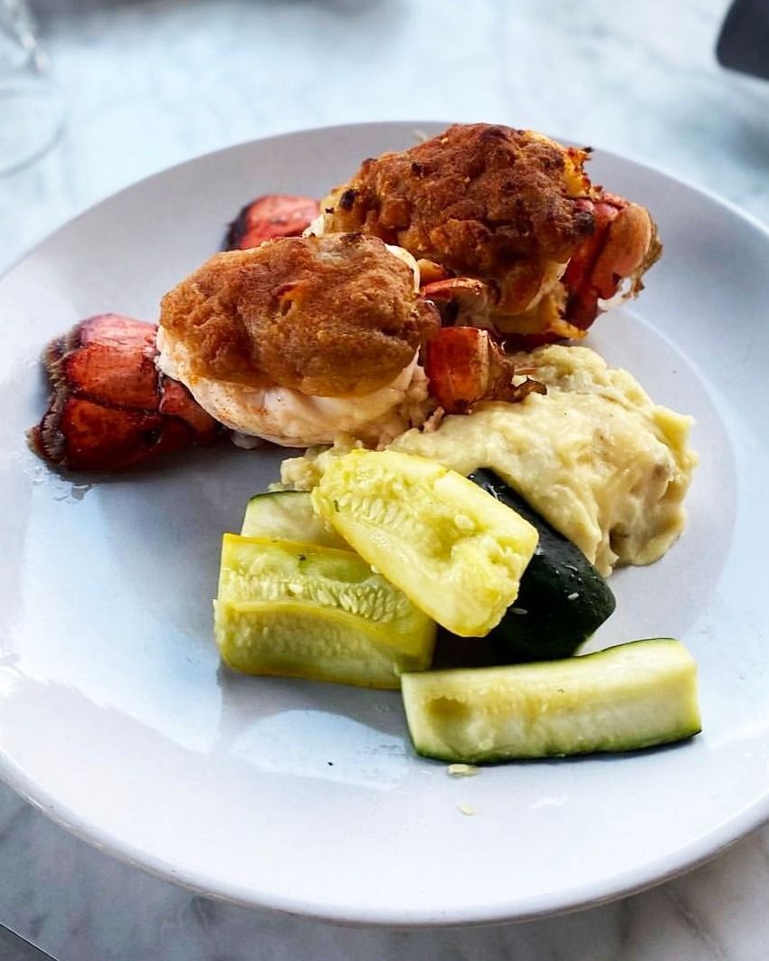 Plate with baked lobster, mashed potatoes, and sliced zucchini.