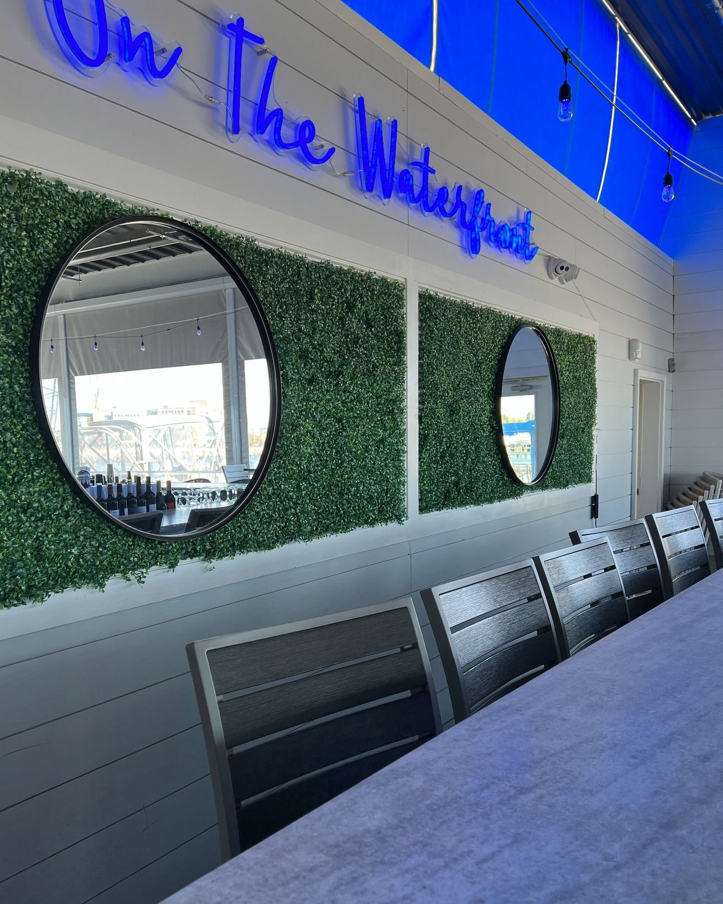 Outdoor bar area with round mirrors, green wall, and blue neon sign.