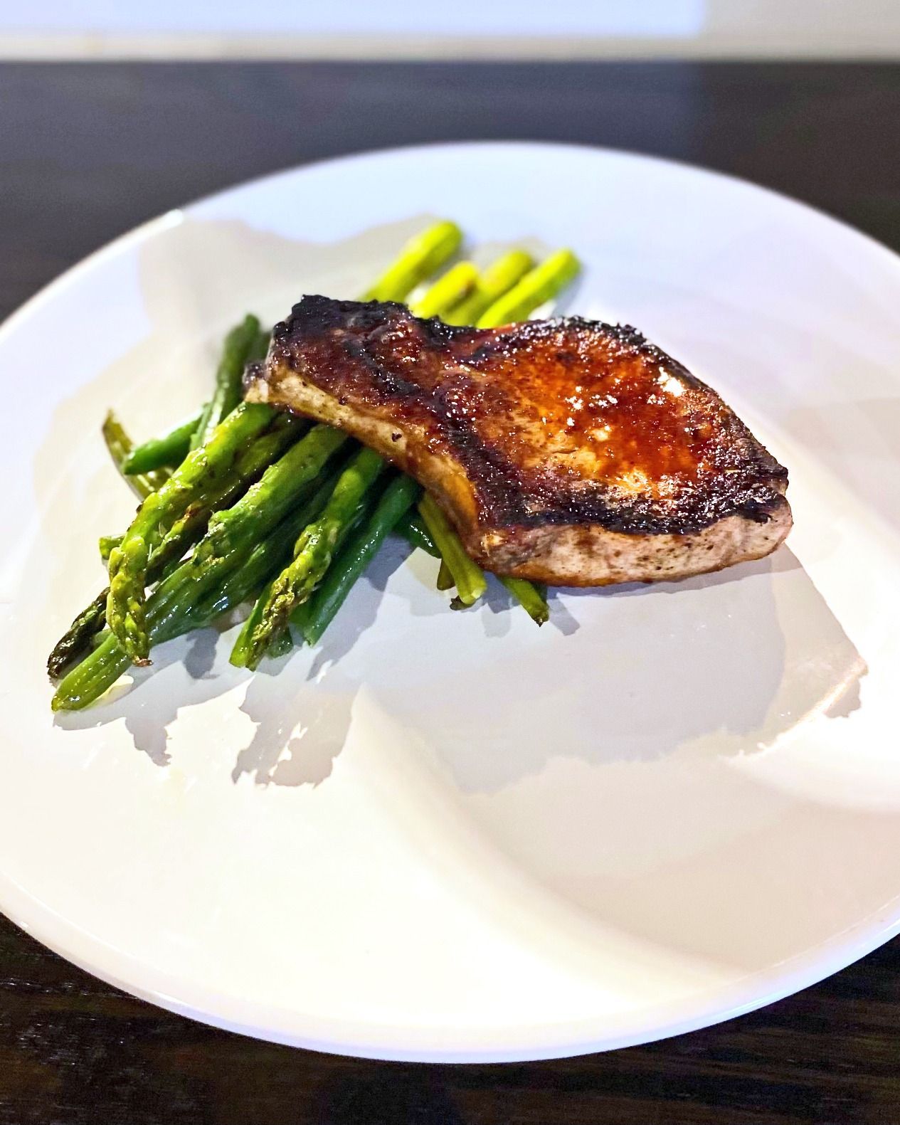 Pork chop with a glazed top and grilled asparagus on a white plate.