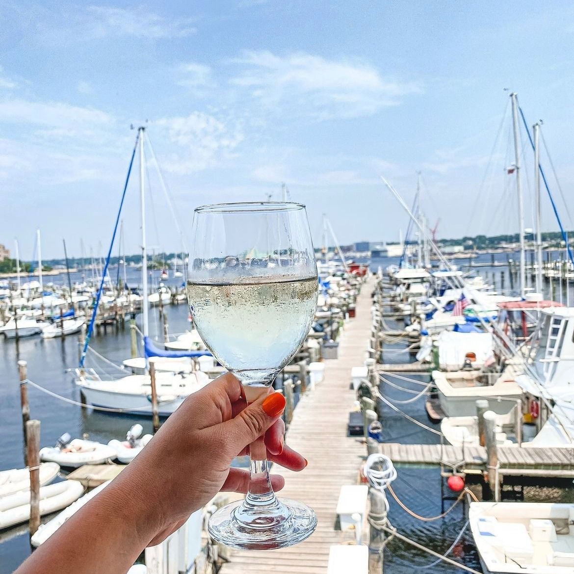 Hand holding wine glass in front of boats docked on a pier.