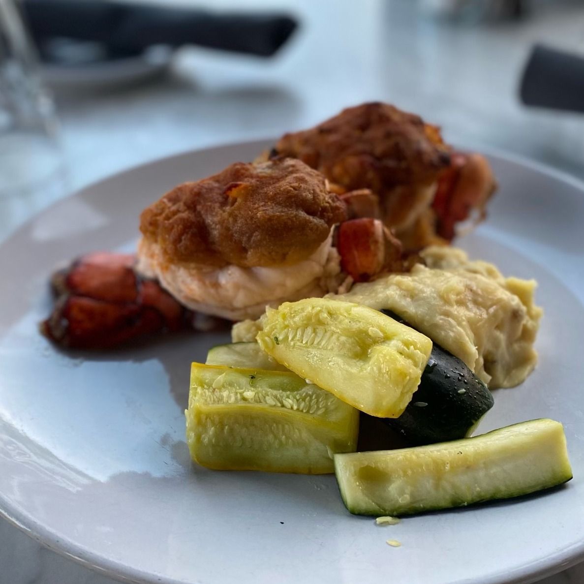 Lobster dish with breaded topping and roasted vegetables on a white plate.