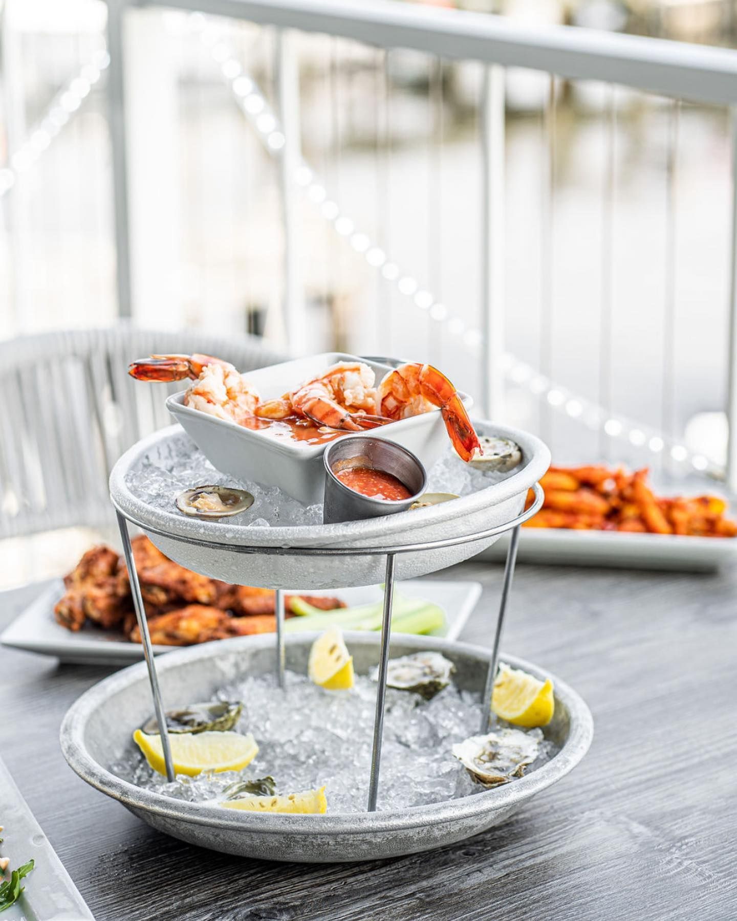Two-tiered seafood tower on ice with shrimp, oysters, cocktail sauce, and lemon slices.