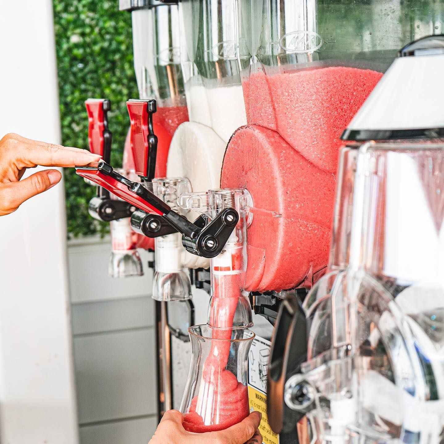 Person dispensing a pink frozen drink from a machine into a glass. Several flavors are available.