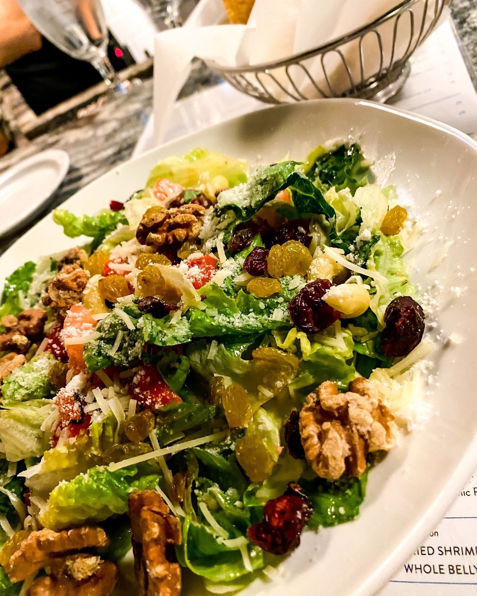 Salad with lettuce, raisins, walnuts, cheese, and tomatoes in a white oval dish.