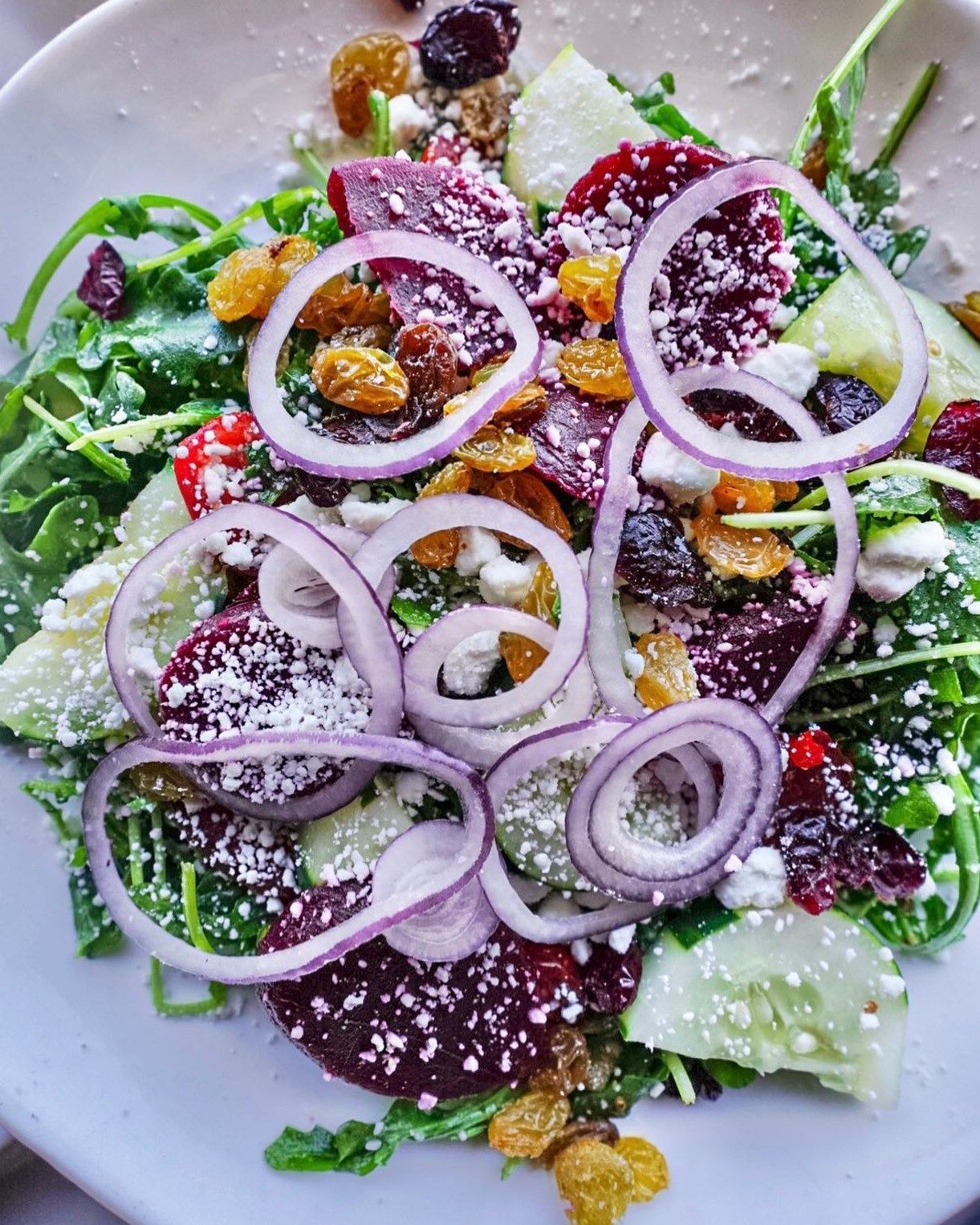 Salad with red onion rings, beets, raisins, cucumber, and goat cheese.